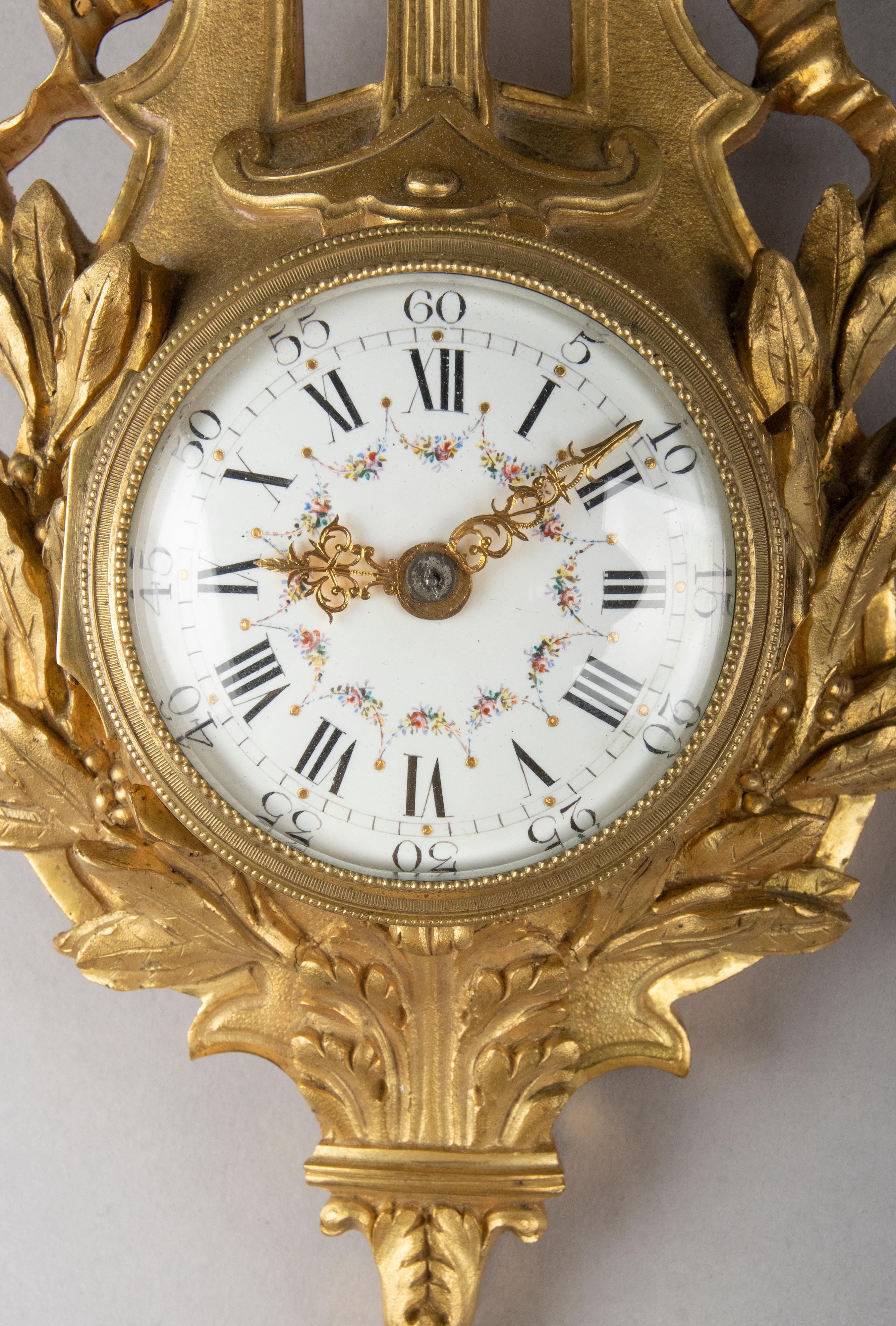 A small and elegant antique cartel clock. The richly chased ormolu case is in the shape of a lyre, with refined details. Ornated in neo-classical Louis XVI style, ribbon with a bow, beaded rim and laurel leaf. The dial is made of enameled copper,