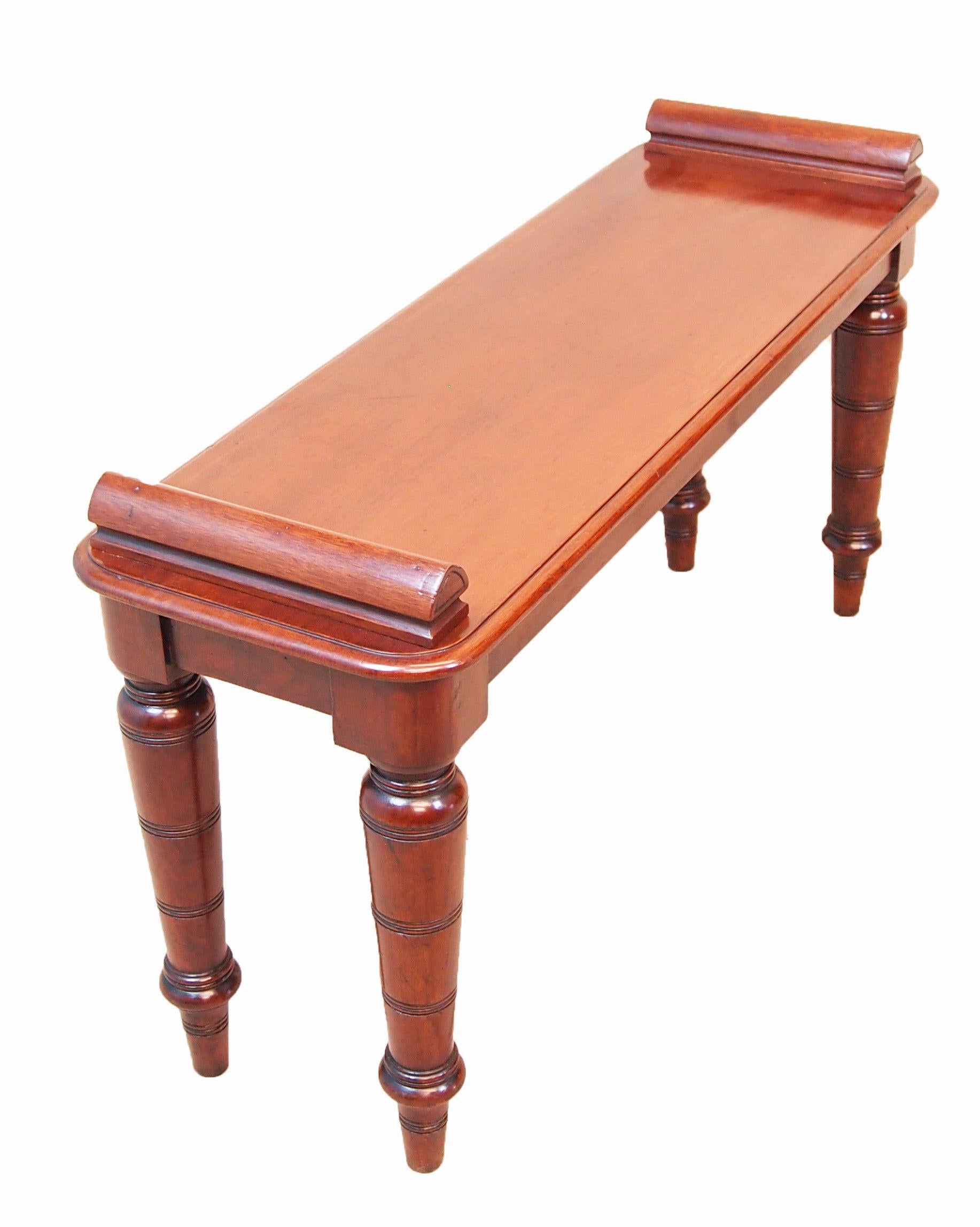 Late 19th Century (1880s) English mahogany hall bench or window seat. It has triangulated rolls on each end of the rectangular top, it is raised on four ring turned tapered legs.
 
