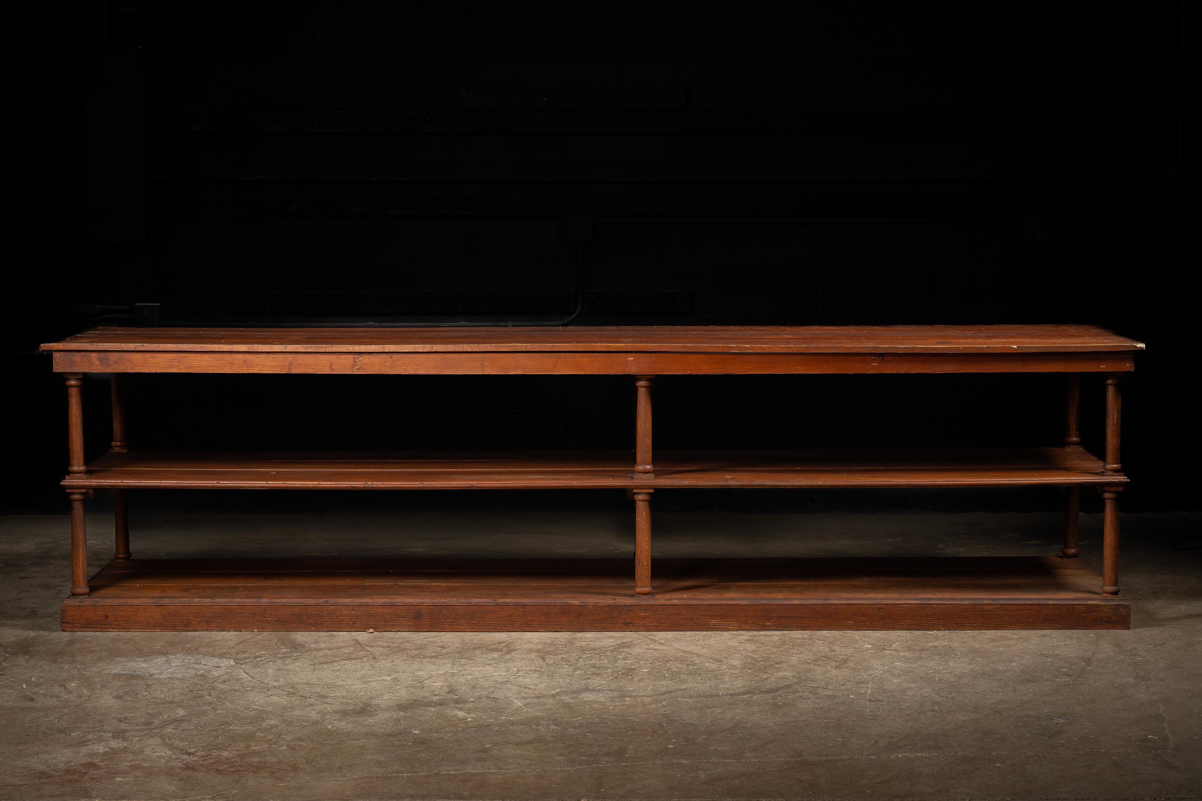 Antique mercantile table or display rack.

This piece trades ornamentation for sturdy, practical design. The table features three tiers of storage separated by simple, turned columns. Each section is completely open, allowing you to reach all the