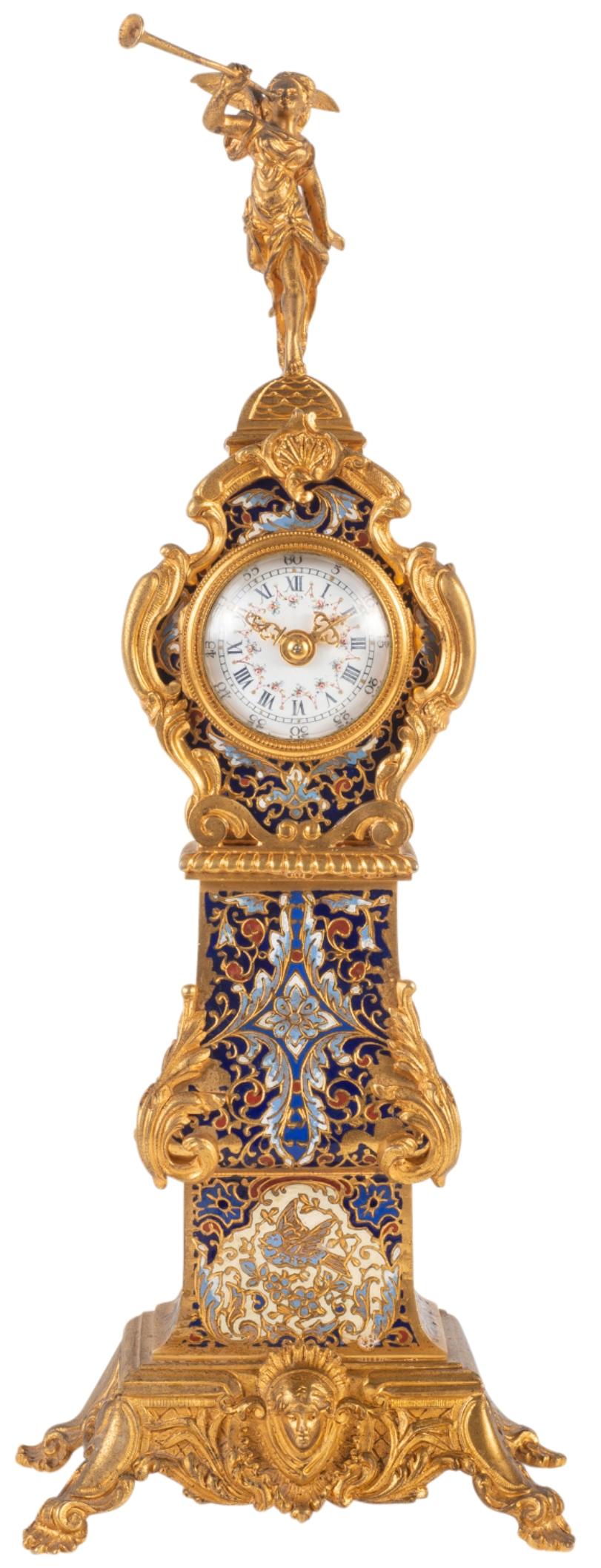 A very good quality late 19th century French gilded ormolu and champlevé enamel mantel clock in the form of a miniature longcase clock. The finial to the top being a cherub blowing a trumpet, foliate C-scrolling decoration, bold blue ground colours