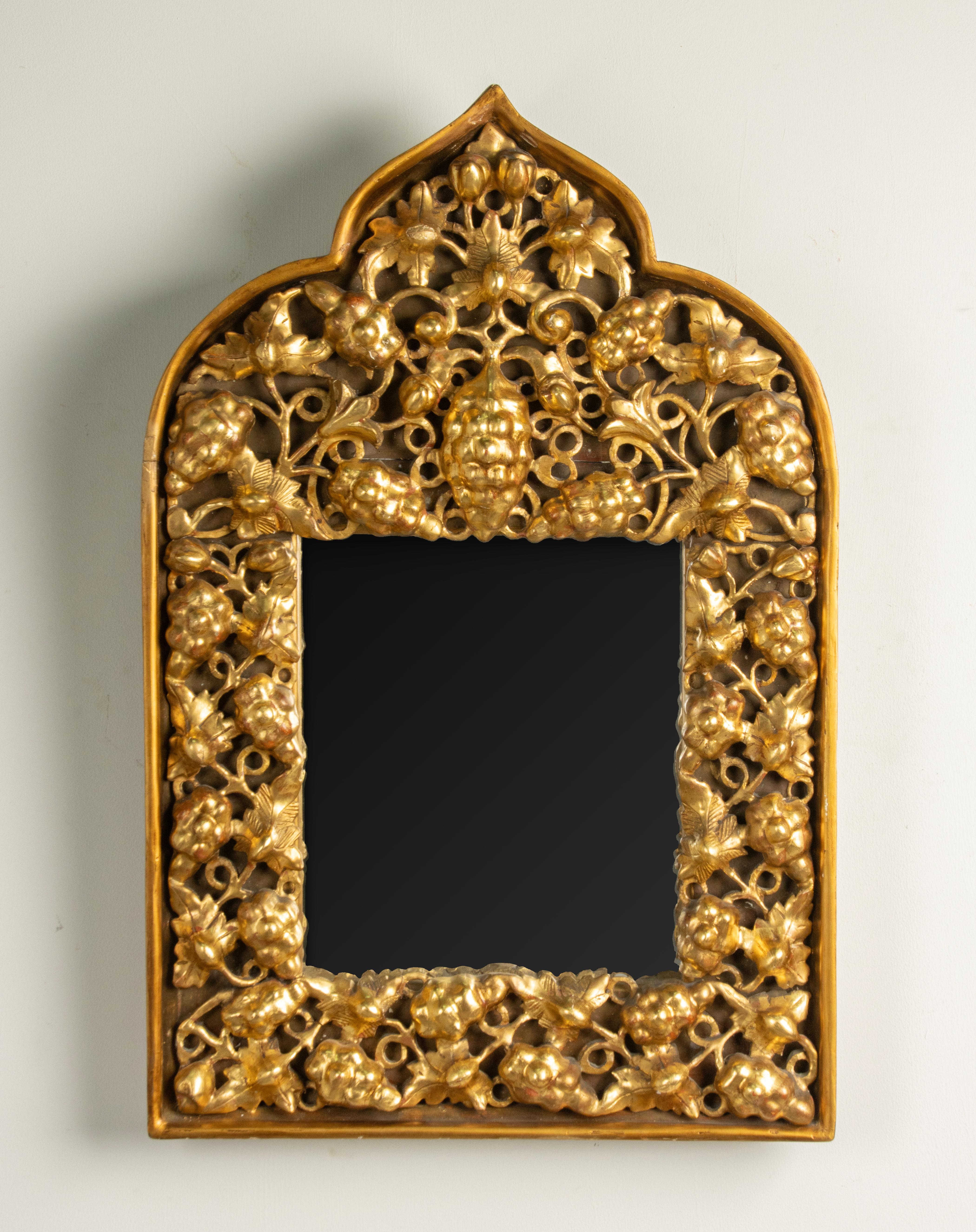 Miroir mural antique doré. Entièrement réalisée en bois sculpté à la main et décorée à la feuille d'or. A l'intérieur, raisins et feuilles de vigne sculptés et ajourés. Son contour est de forme orientale (arabe ou tibétaine). Probablement fabriqué