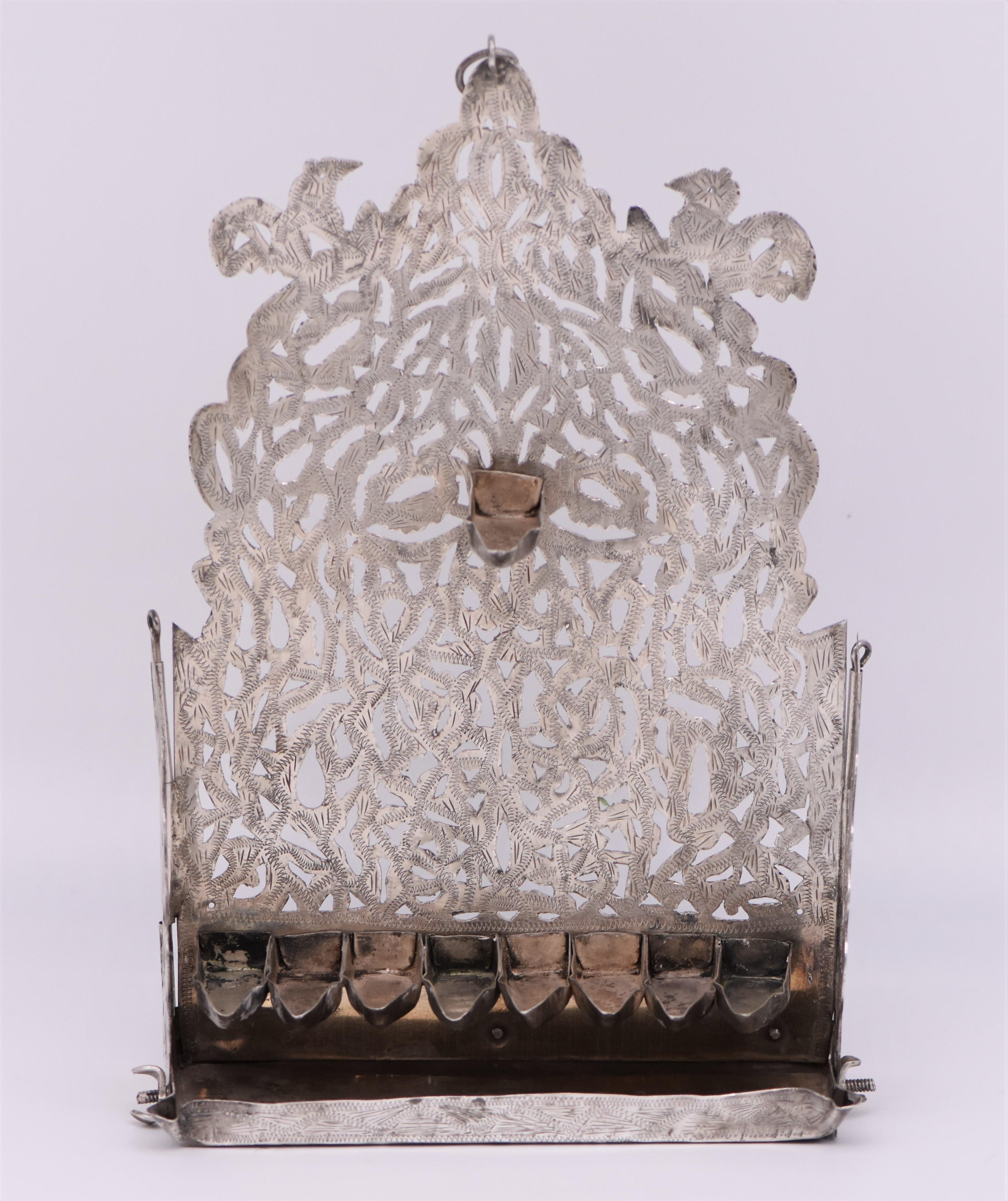 Silver Hanukkah lamp, Morocco, circa 1880. Cut and chased silver, stamped with Moroccan silver hallmarks. This beautiful hanging oil lamp is cutout with a decorated and engraved back plate. Two pillars on the sides with flanking roosters and two