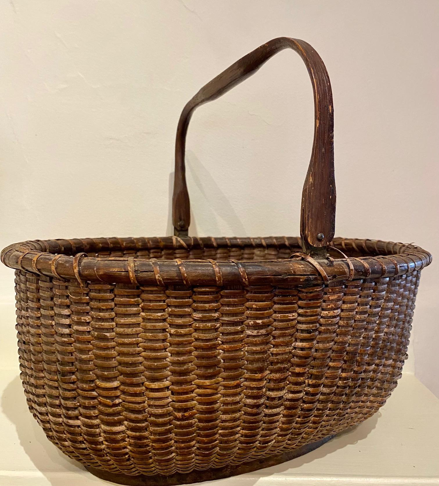 Late 19th century nantucket basket, by Mitchy Ray (1877 - 1956), circa 1920s, a large open oval basket with heavy rattan staves, cane weave, solid oak bottom plate and carved swing handle attached to fairly long metal ears. The basket is unsigned