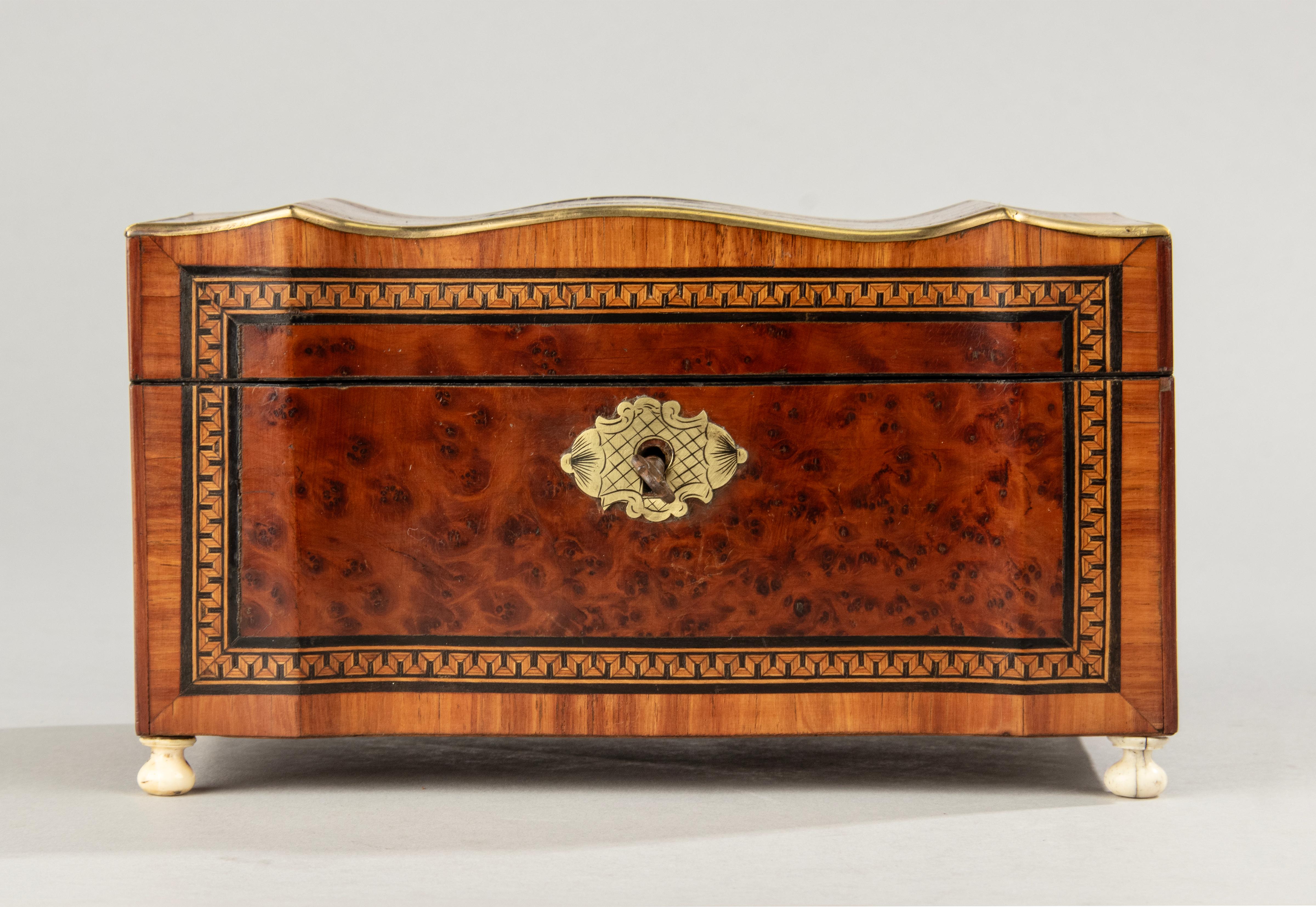 Ancienne boîte à thé française de style Napoléon III, avec un couvercle courbé en forme d'arbalète. La boîte est plaquée de différentes essences de bois, de ronce de noyer. Le couvercle est incrusté d'une garniture en laiton. A l'intérieur, deux