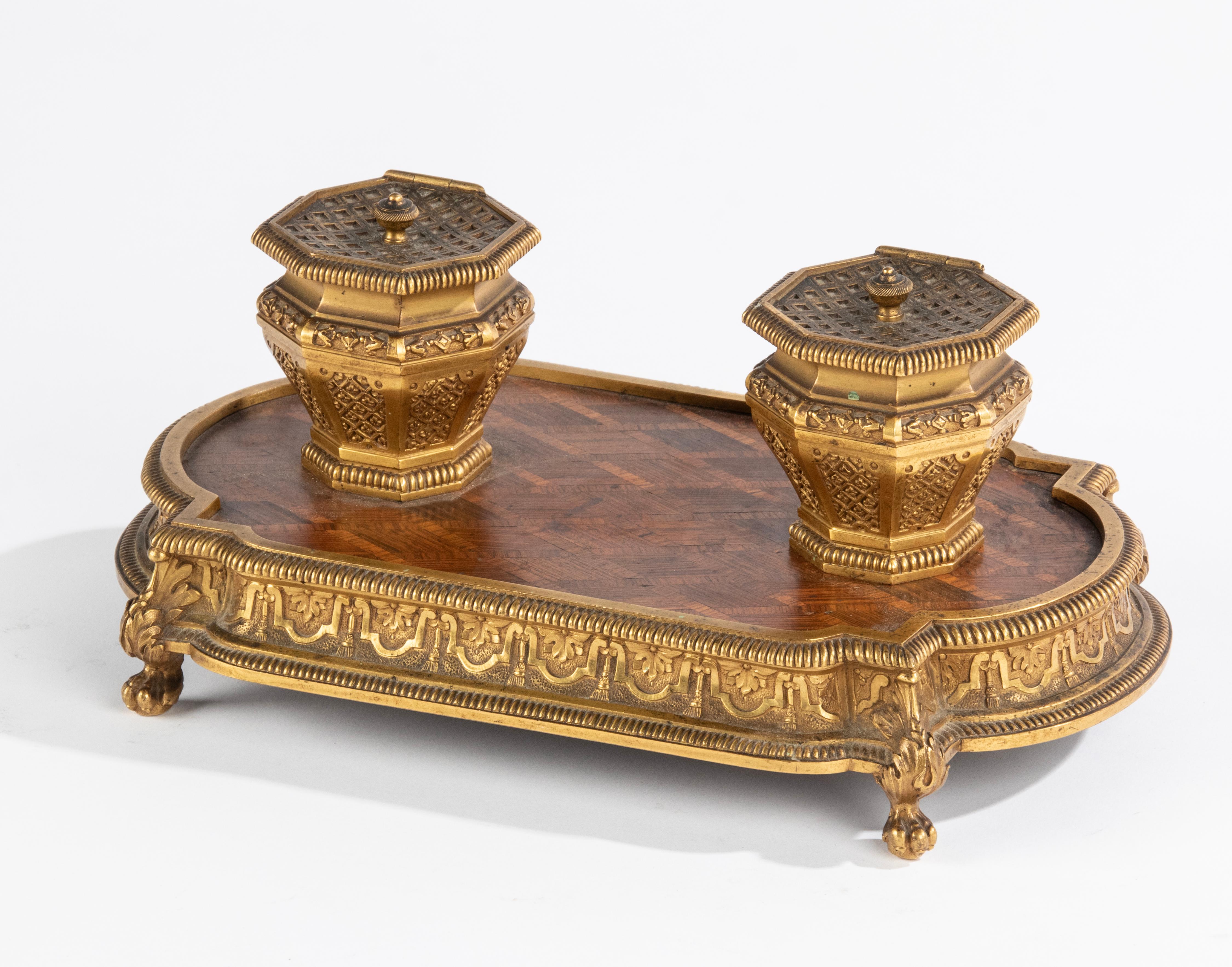 A refined antique inkwell, with two inkwells made of bronze, including glass cups. The base is made of veneered marquetry wood with a diamond pattern, framed in a bronze rim, resting on clawfeet. Nice classic desk accessory. Made in France, at the