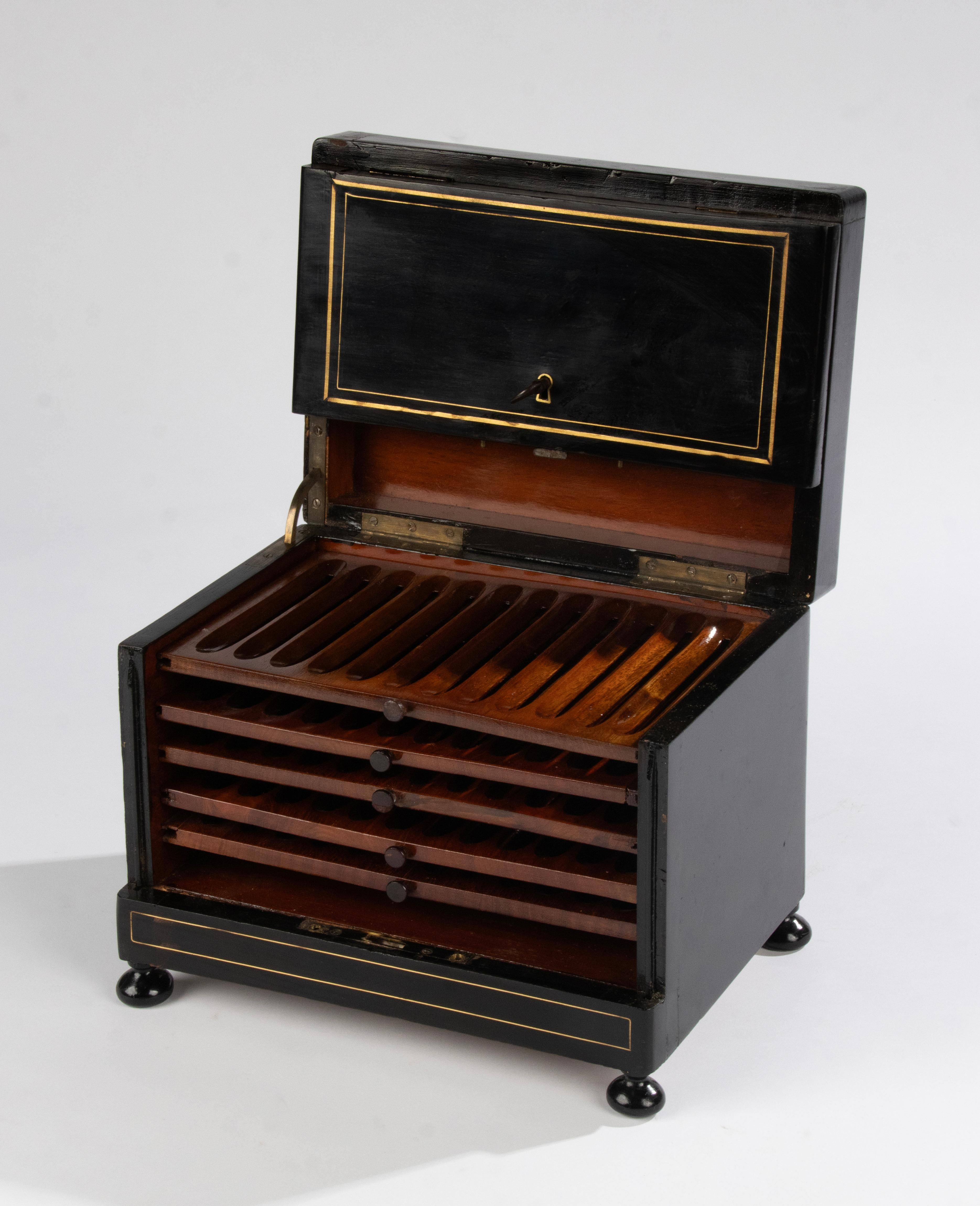 A stylish Napoleon III cigar cabinet, crafted with ebonized wood, brass inlays, and a distinctive medallion at the top, this late 1800s piece reflects the refined style of the Napoleon III era. Inside, organized compartments with five drawers, space