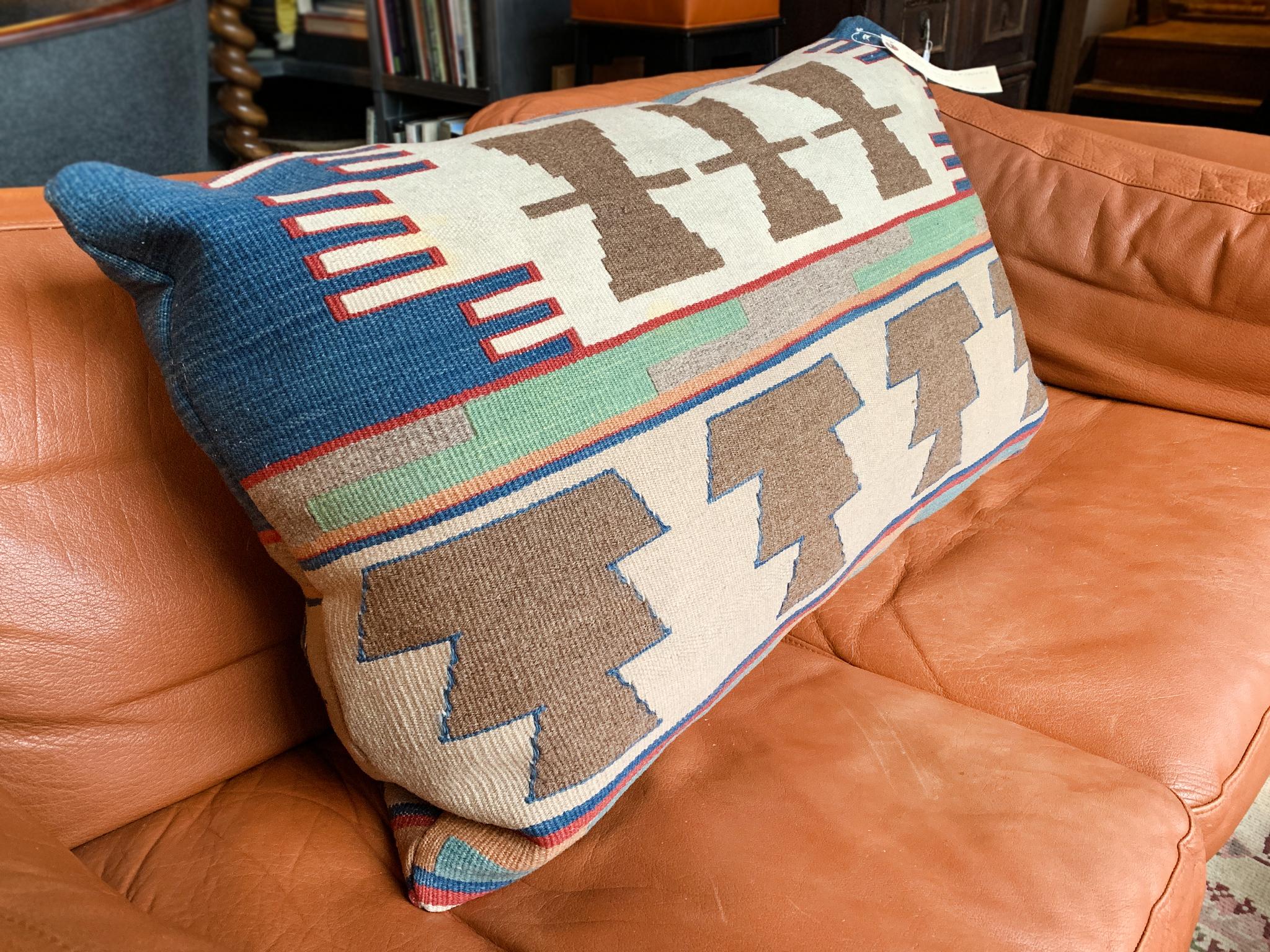Questo cuscino è stato realizzato su misura a partire da una coperta di lana Navajo della fine del XIX secolo. Il tessuto è intrecciato a mano in un disegno a righe e motivi geometrici, in un'audace tavolozza di blu, rossi, marroni, verdi, arancioni