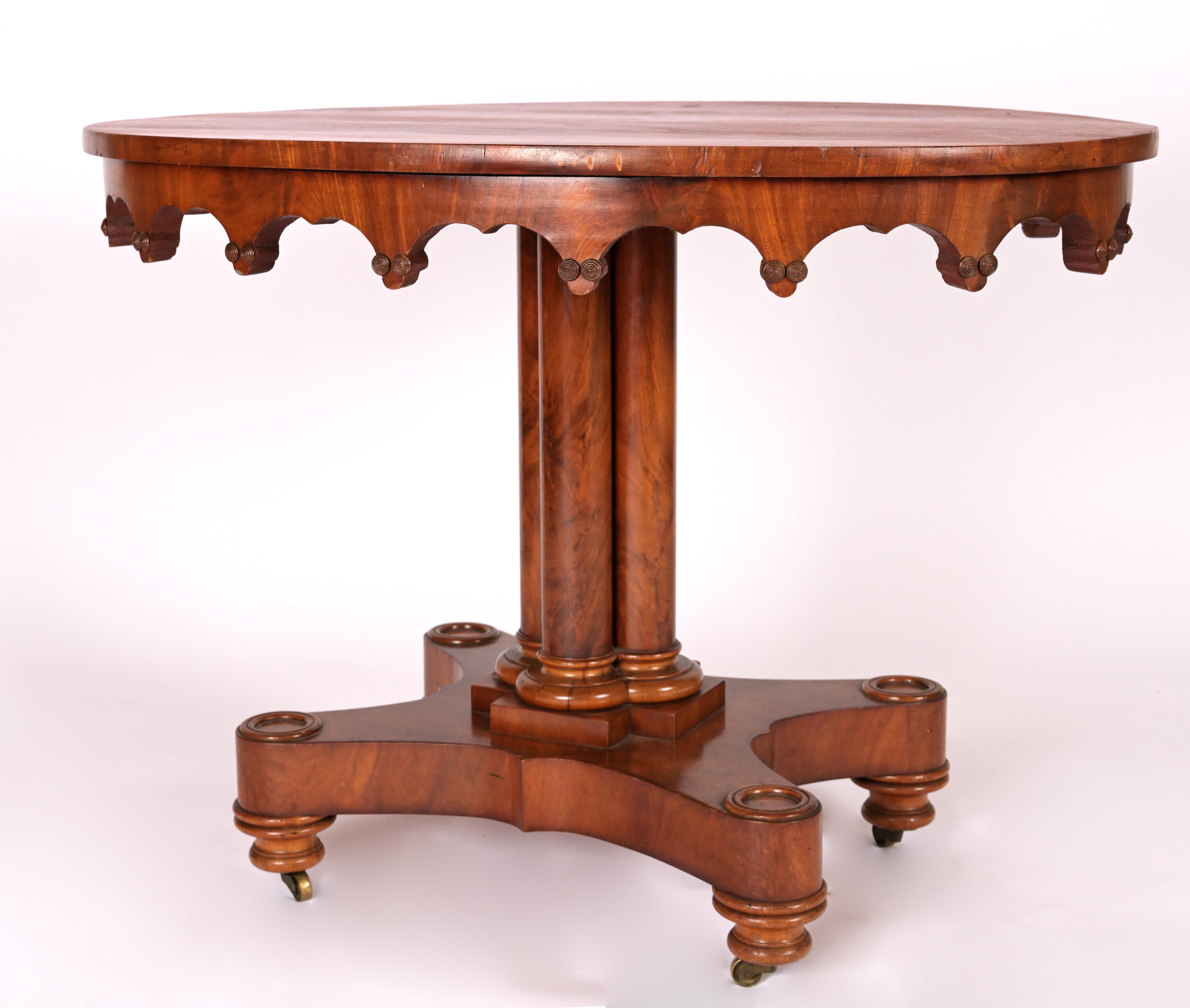 Mahogany Neo-Gothic center table with sharp downward carvings and stem base with four extruding stands. Circa 1830.