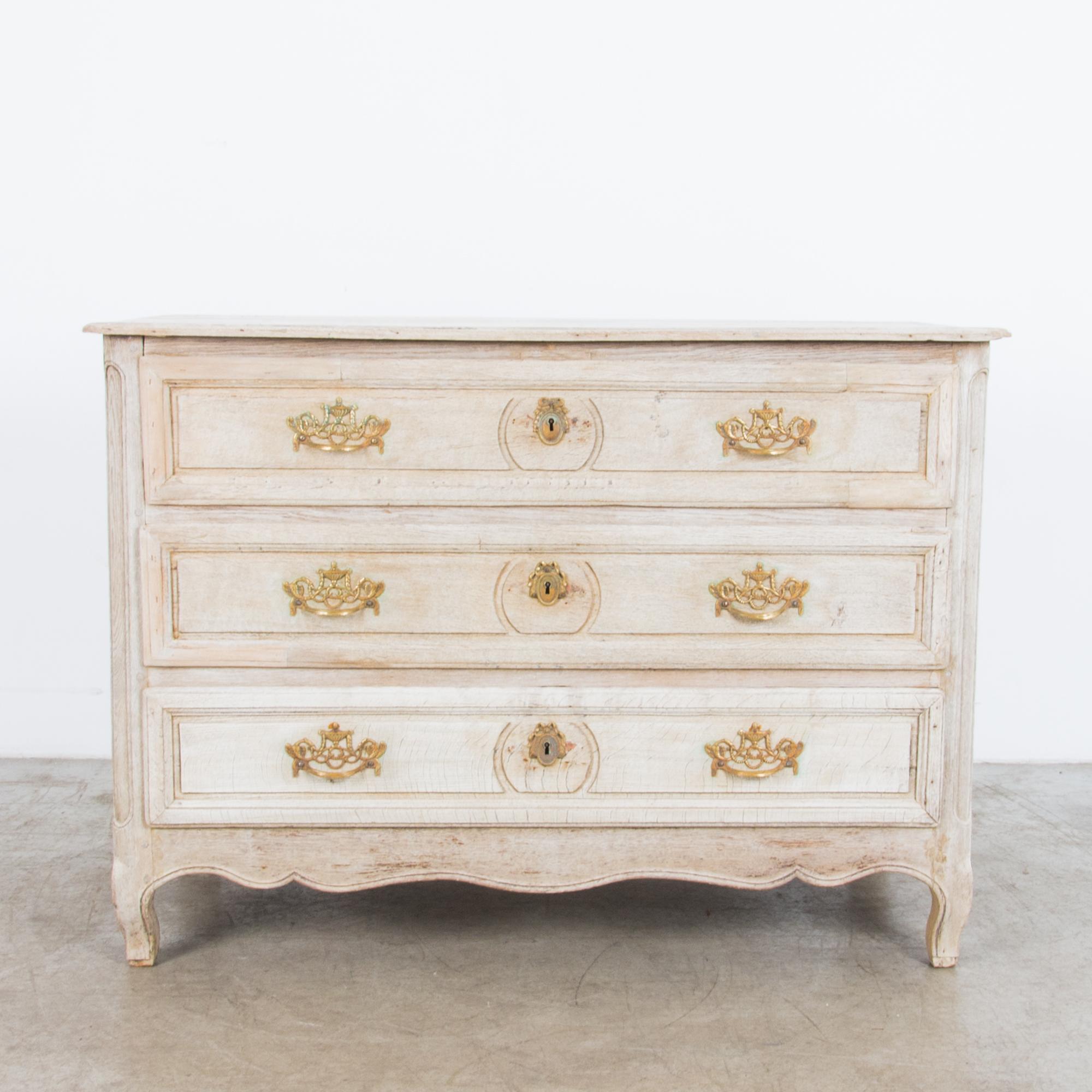 This antique chest of drawers from 1880s France is made of oak, restored and refinished for a bright contemporary effect. It features a gently Rococo silhouette and three pull-out drawers bearing elaborate gilded lock-pieces and drawer handles. The