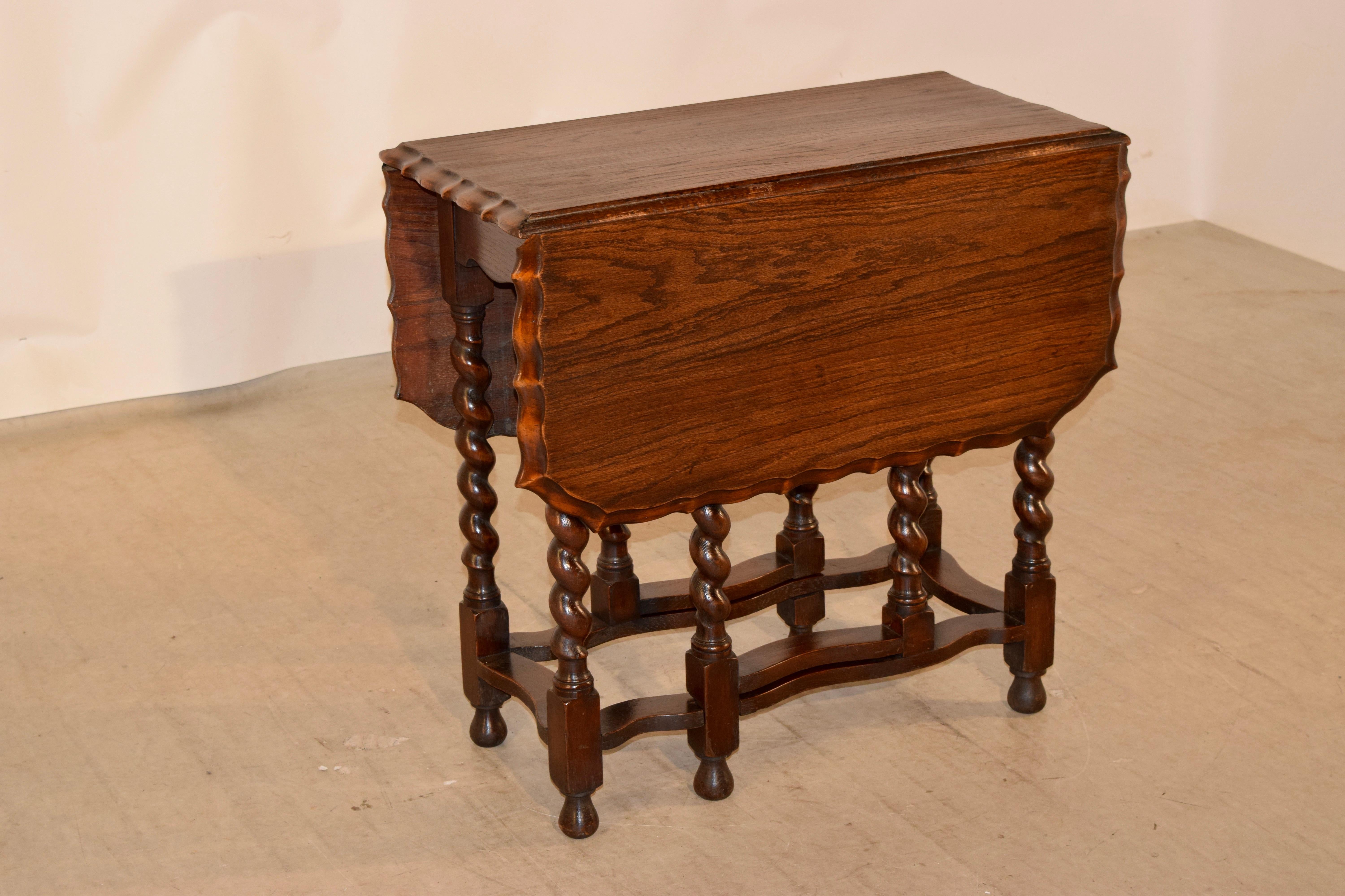 Late 19th century English oak gate leg table with a beautifully scalloped and beveled edge around the top following down to a simple apron and supported on hand-turned barley twist legs. The legs are joined by serpentined stretchers and supported on