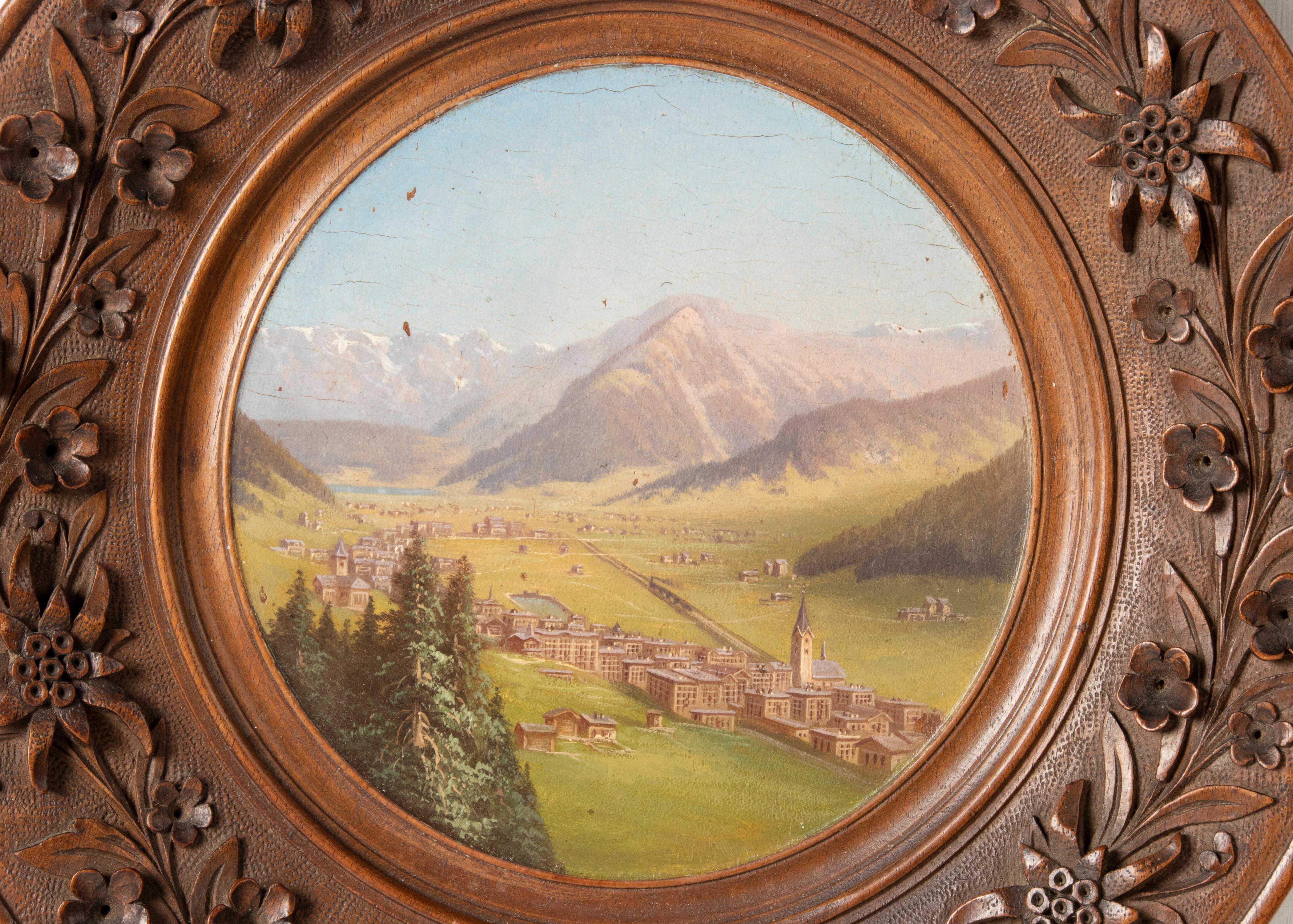 A antique painting of an alpine landscape in a wooden Black Forest frame. The painting shows a Swiss village in a valley. It is beautifully painted with soft color use. The frame is hand-carved with floral motifs, typically Black Forest.
There is a