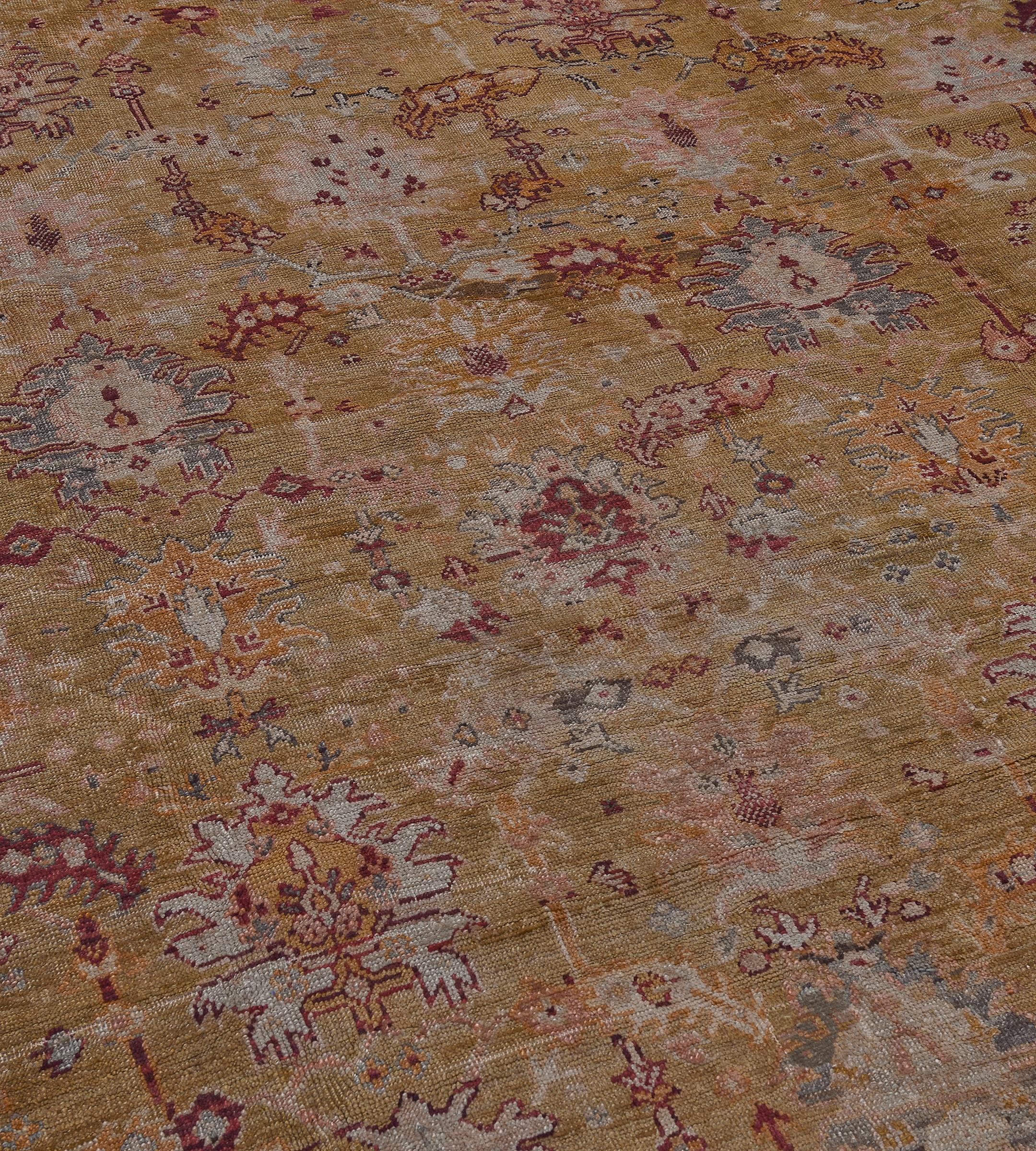 Questo antico tappeto turco Oushak ha un campo verde pistacchio con un disegno generale di palmette rosa polveroso, azzurro e rosso bordeaux, collegate da una vite angolare stilizzata di fiori e foglie e circondate da motivi floreali angolari