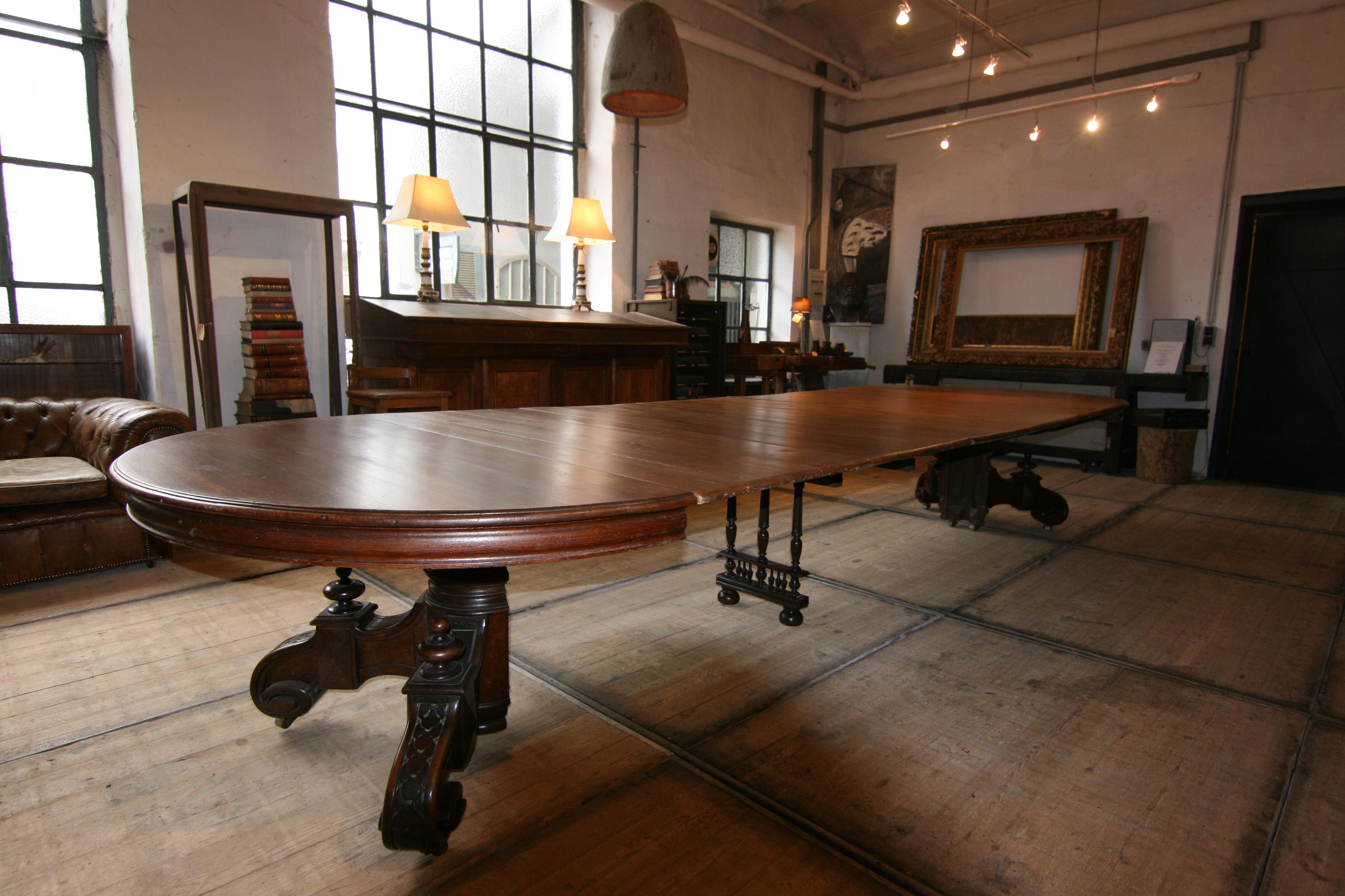 A large late 19th century oval extending table made of oak. Standing on a 2-part carved metatarsus with brass castors with a total of 5 extension plates (leaves partially made of pine). The table can be extended to a maximum length of 450 cm or