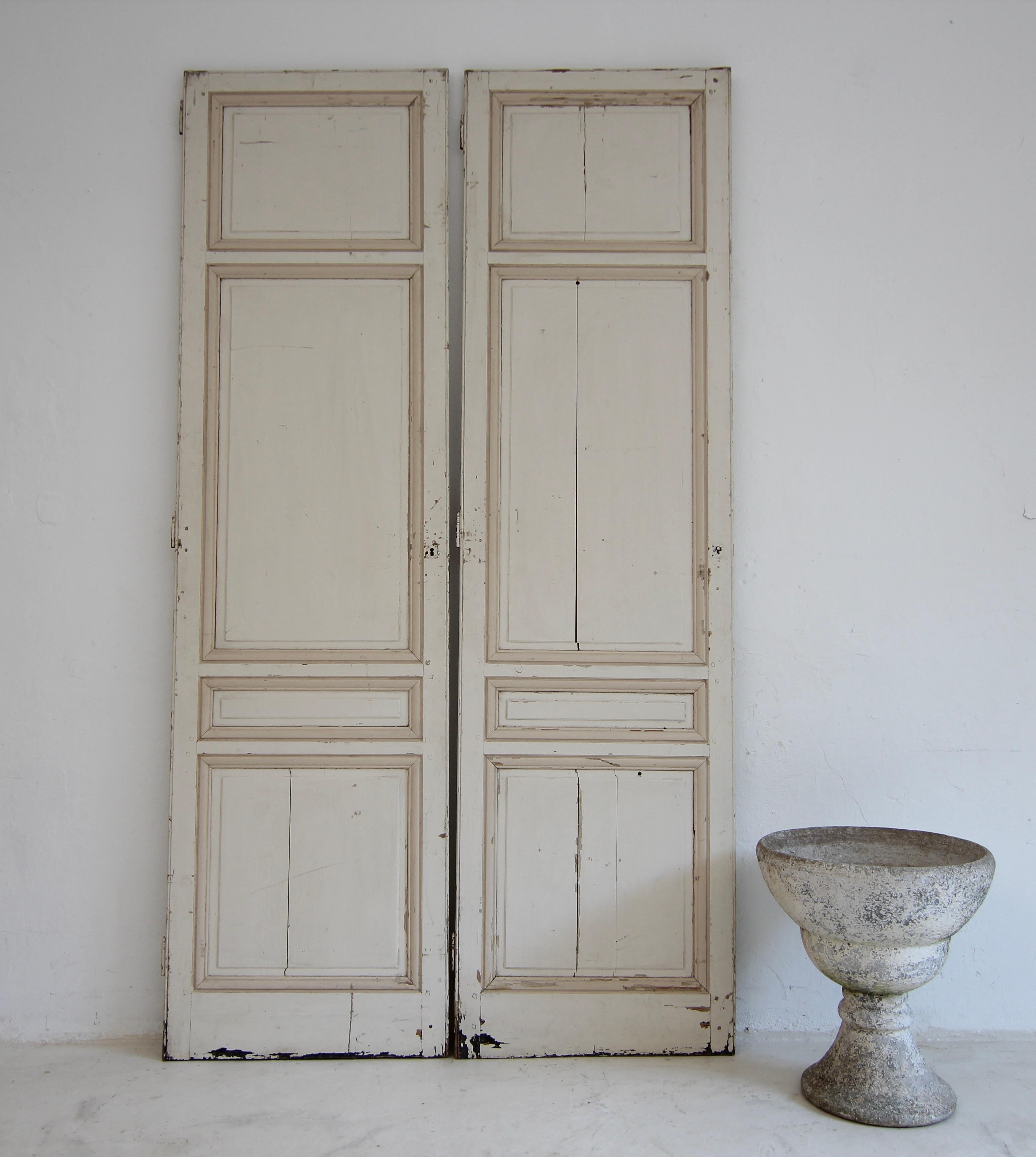 A pair of late 19th century doors from a built-in cupboard. Unrestored with original painted finish in light cream with dark cream contrasting profiles.

Made of pine wood in frame and panel construction, each with 4 cassettes and external hinges on