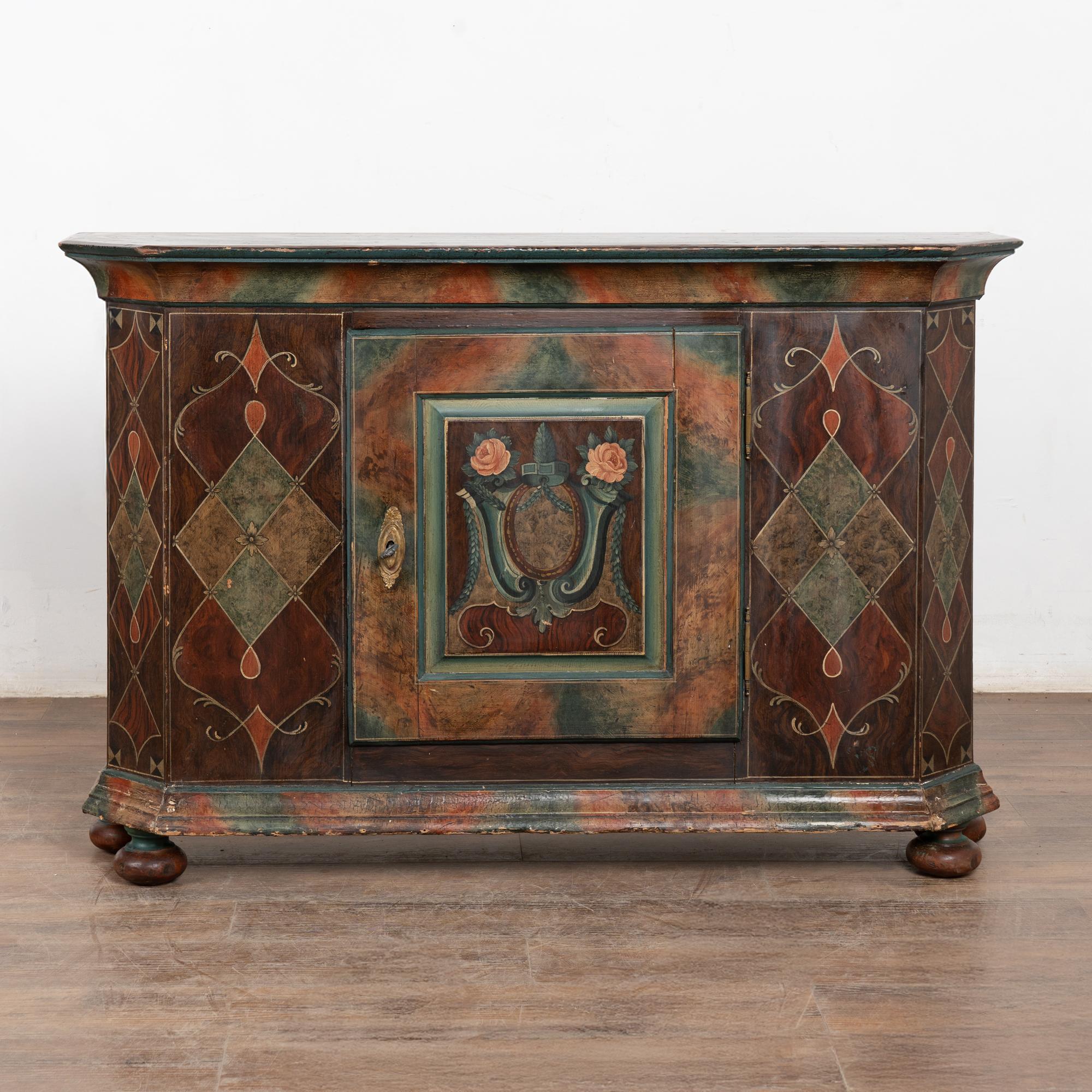 This narrow console has an Italianesque feel, due to the stylized paint which is old but not original to this pine sideboard from Hungary. Lovely marbleized earthtones, flowers, and geometric flourishes captures the eye. 
The original lock still