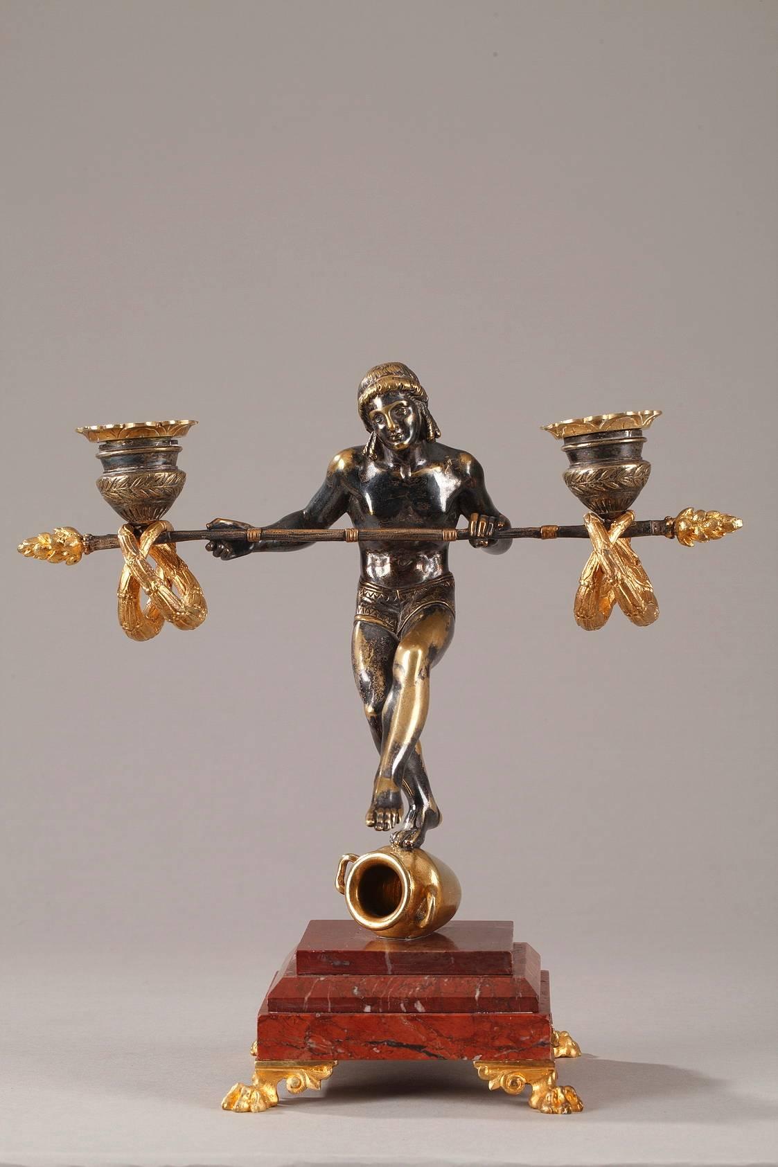 Original pair of gilt bronze candlesticks decorated with Greek acrobats. They are poised on Amphora, holding balancing rods which support garlands and the candle sockets. The candlesticks are set on square, red marble bases above four gilt bronze