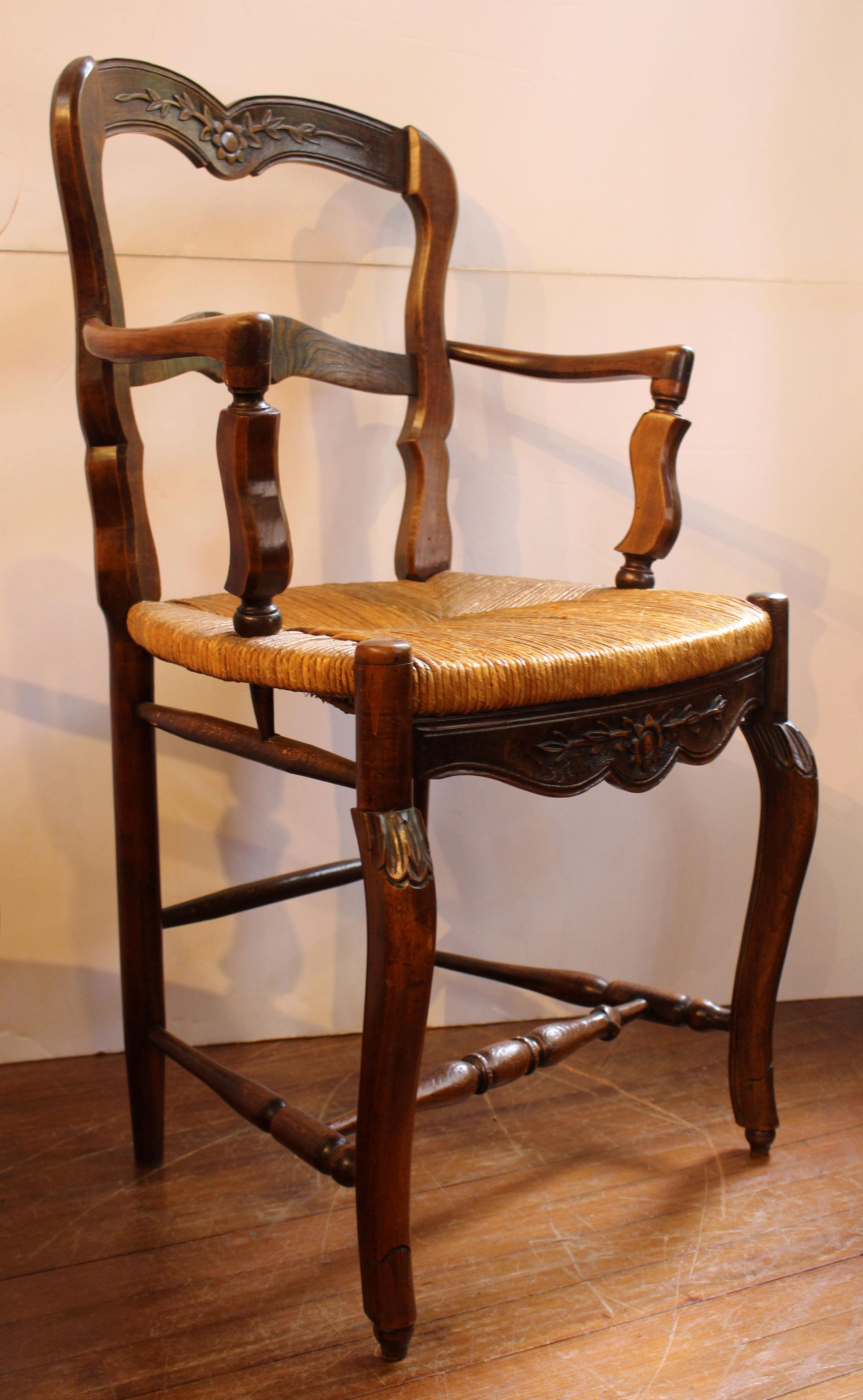 Late 19th century pair of country French Louis XV style fauteuils (arm chairs). Elm & ash with rush seats. Shaped ladder back. Crest rail & front seat rail carved with a sunflower & tendrils. Modified cabriole legs with carving ending in onion feet.