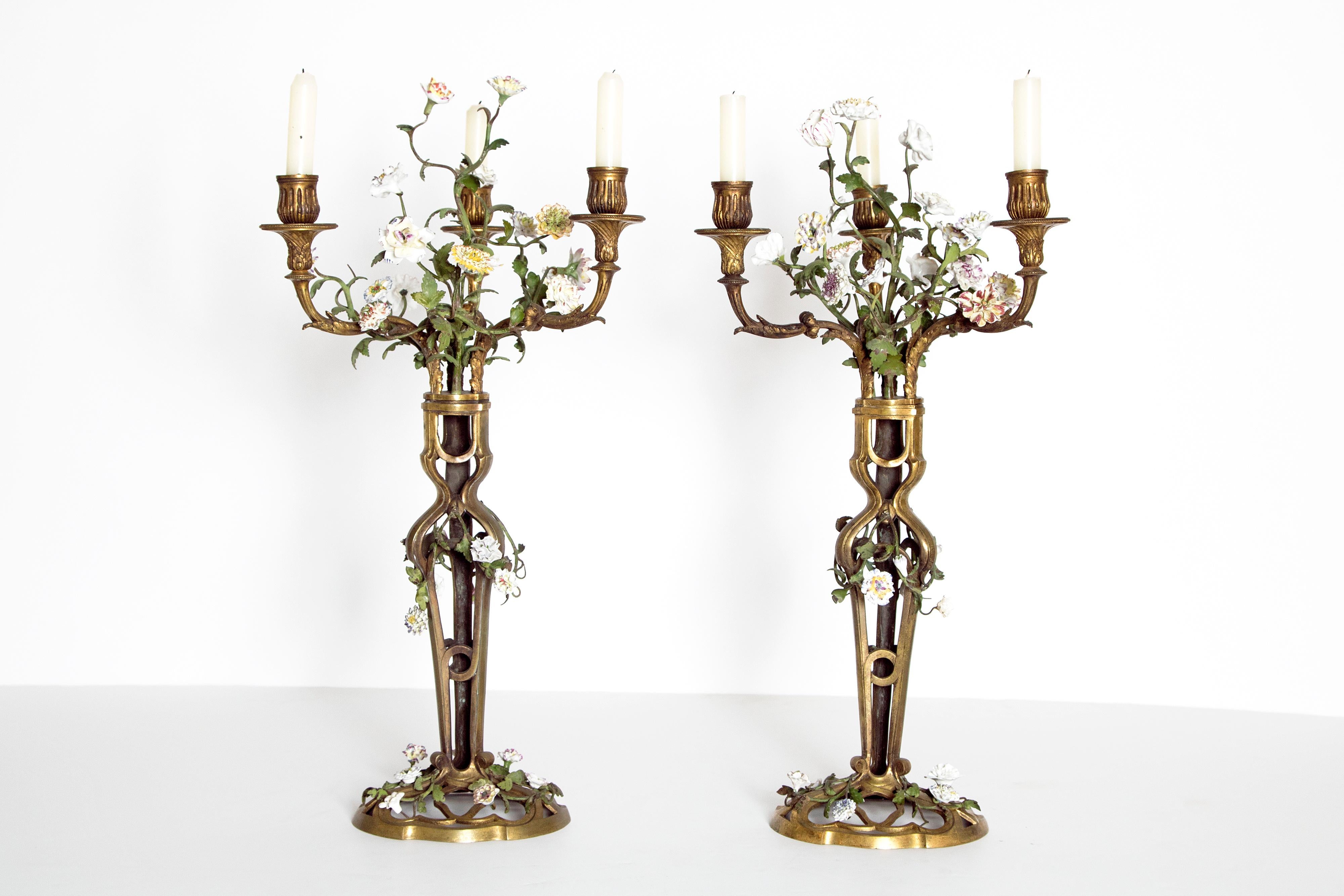 A whimsical pair of French gilt bronze candelabra with a filigree base and stems. Each candlestick has three arms. Applied overall bouquets of porcelain flowers on metal green stems with leaves. As found, late 19th century, France.