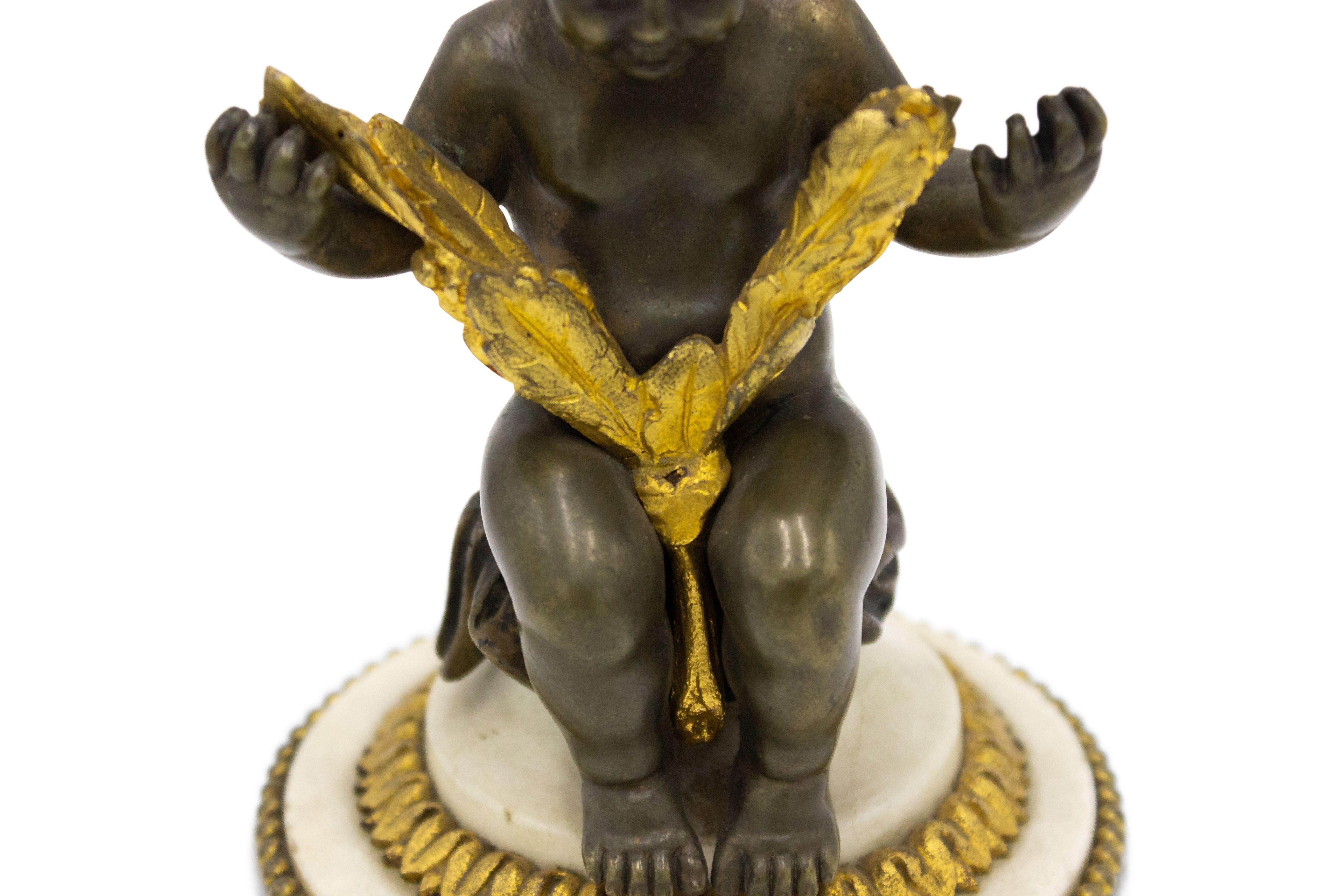Pair of French Victorian bronze seated cupid figures holding gilt leaves with gilt trim on round shaped white marble base.
 