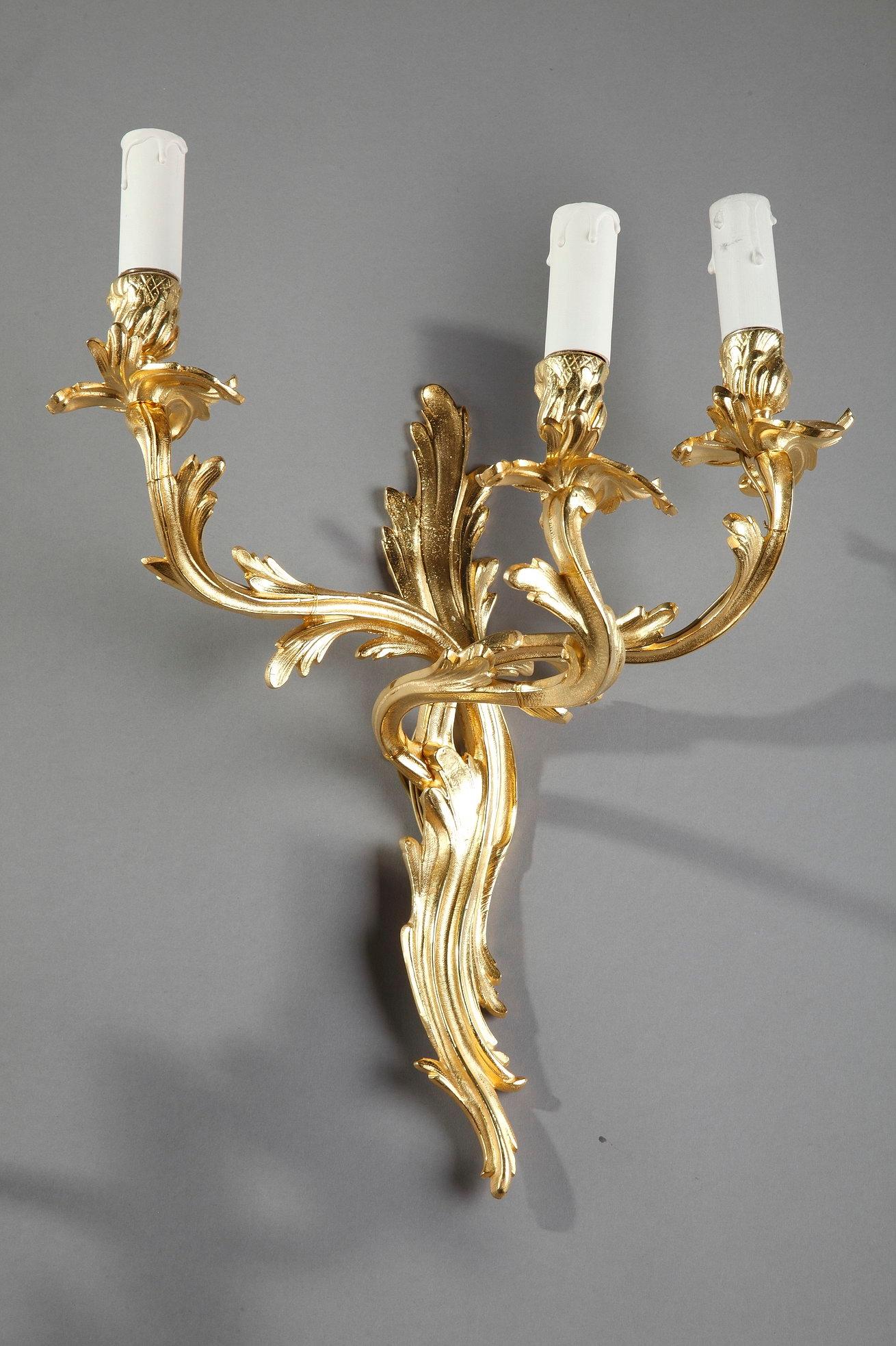 French wall sconces in gilt and chiseled bronze with two lights, richly decorated with flowing and asymmetrical foliage in Louis XV style. This rich and asymmetrical rococo-inspired decoration was widely imitated in the second half of the 19th