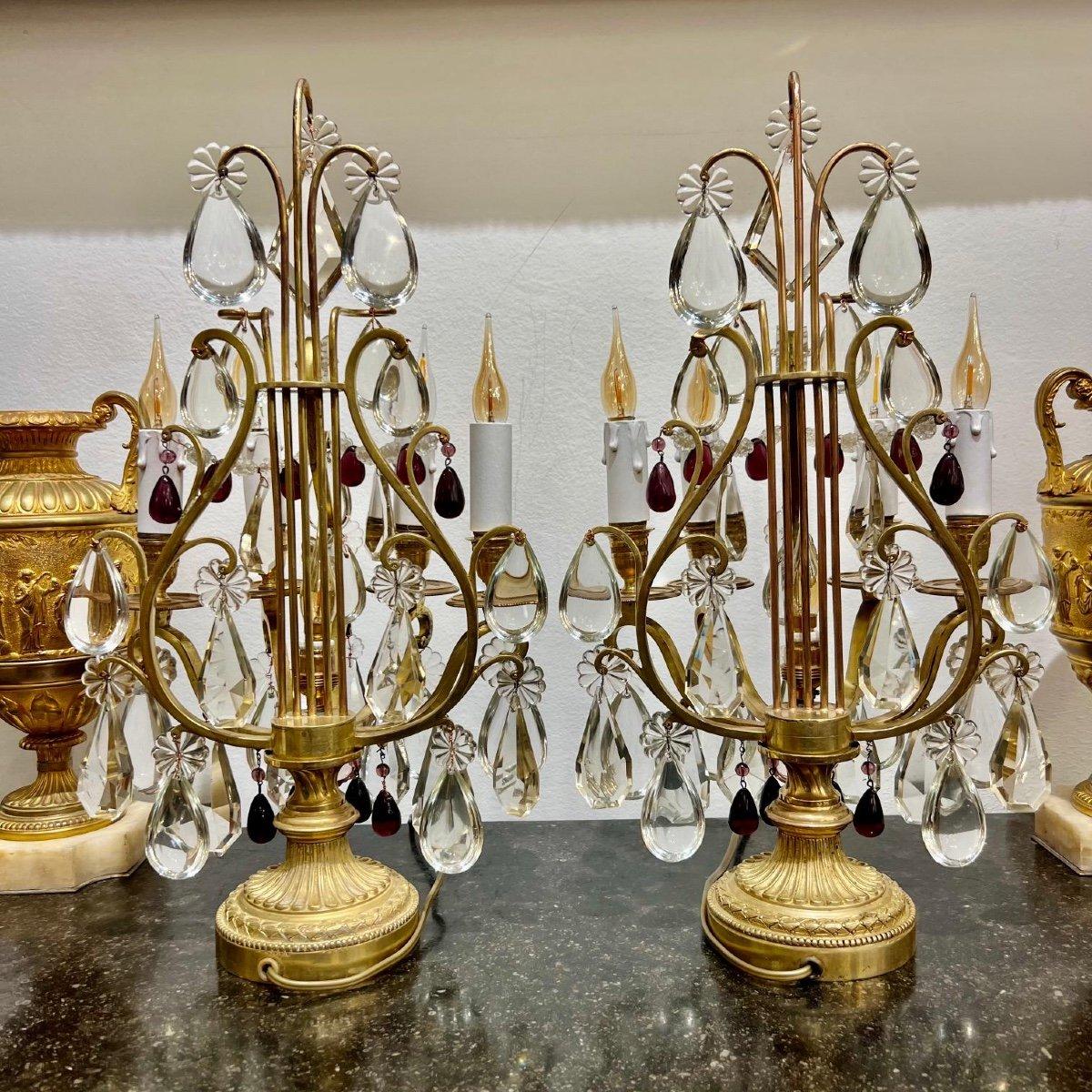 This stunning pair of candelabras is made of gilded bronze and crystal, consisting of four lights each. The gilded bronze structure is designed in the shape of a lyre, adding a touch of classical sophistication to any space. They are adorned with