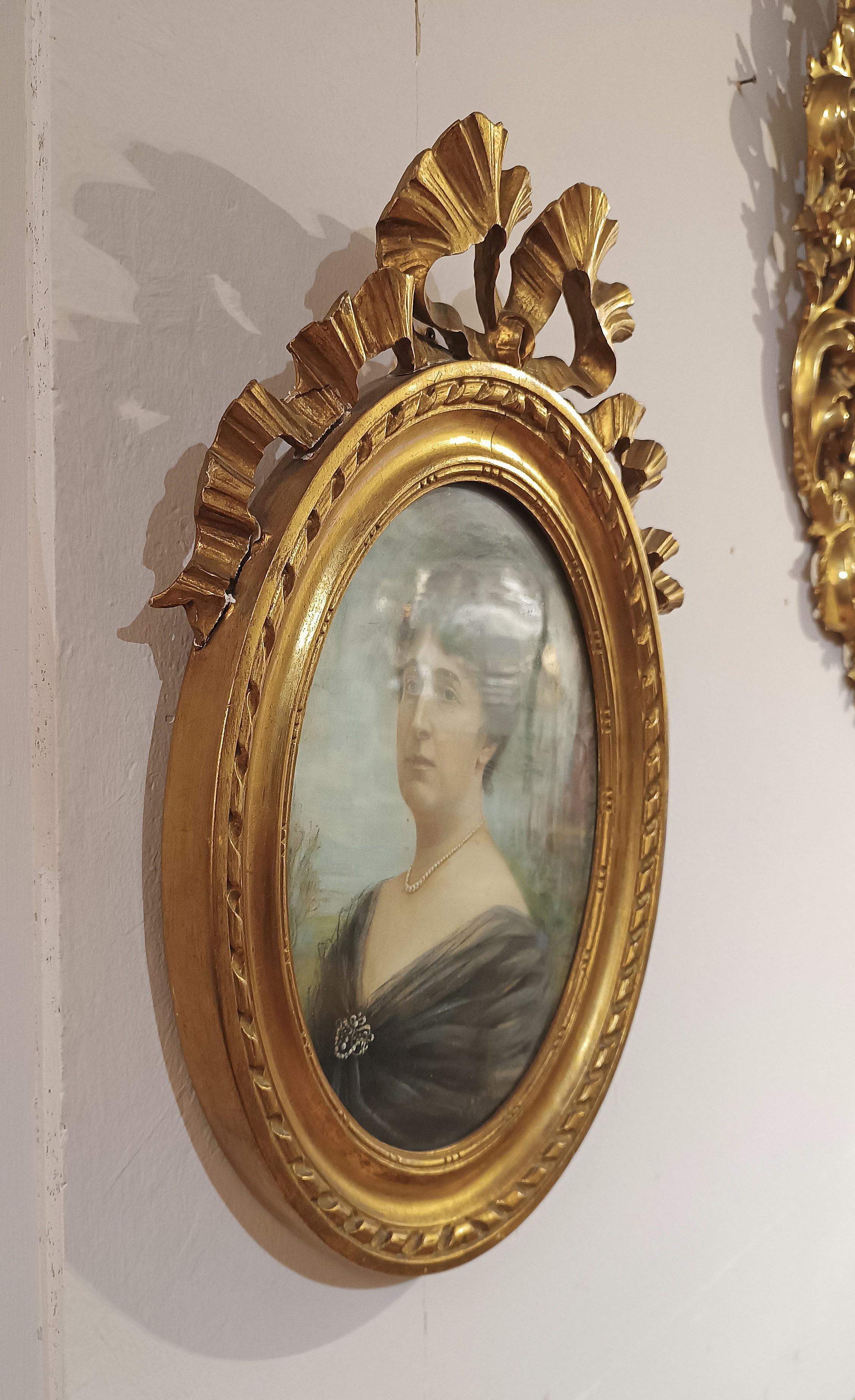 Elegantes Paar ovaler Gemälde, die in Pastell auf Papier gemalt und in geschnitztem, vergoldetem Holz gerahmt sind. Die exquisiten Rahmen, die oben mit Bändern verziert sind, beherbergen zwei Porträts zweier Frauen vor einem Landschaftshintergrund.