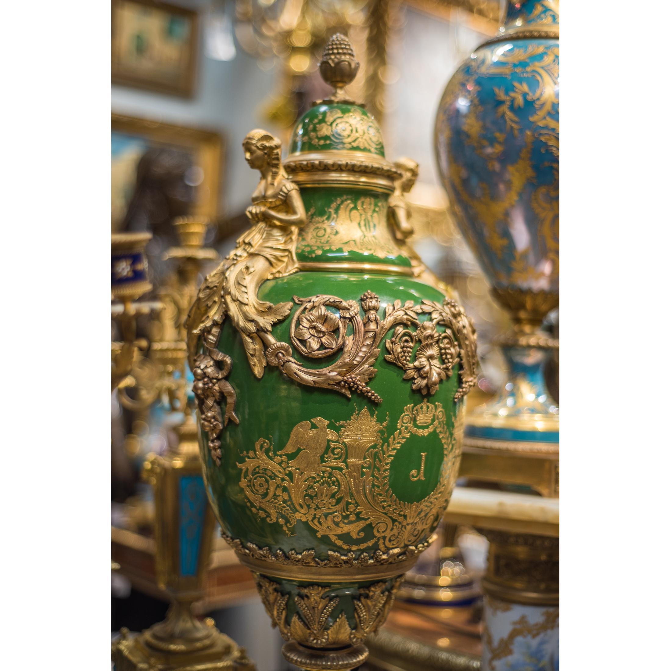 A fine quality pair of Sèvres style porcelain urns and cover. Each green with gilded highlights, domed top over baluster-form base decorated with an 