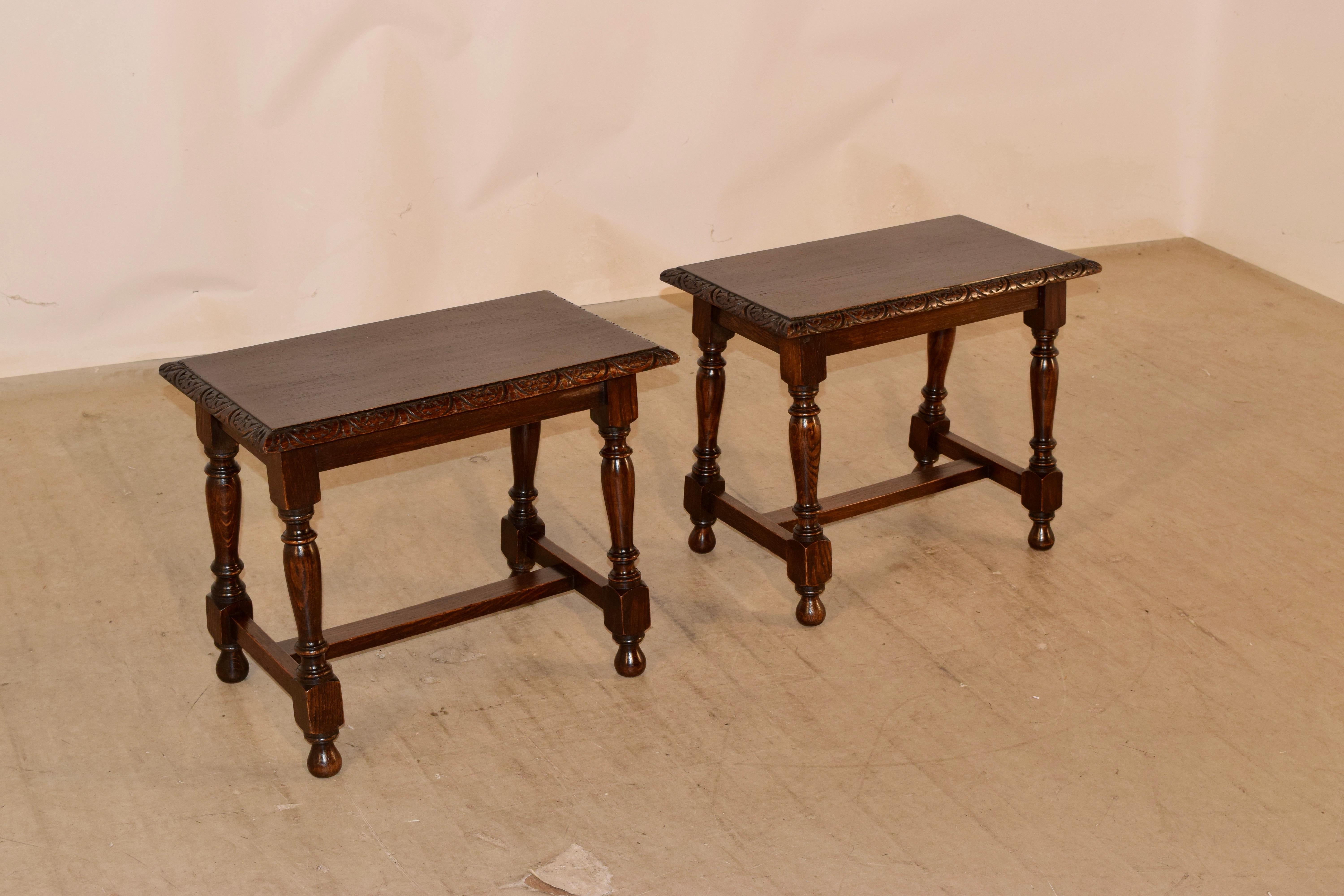 Late 19th century pair of oak stools from England with a beveled and carved decorated edge around the top, following down to a simple apron and supported on splayed turned legs, joined by simple cross stretchers. The stools are raised on hand turned