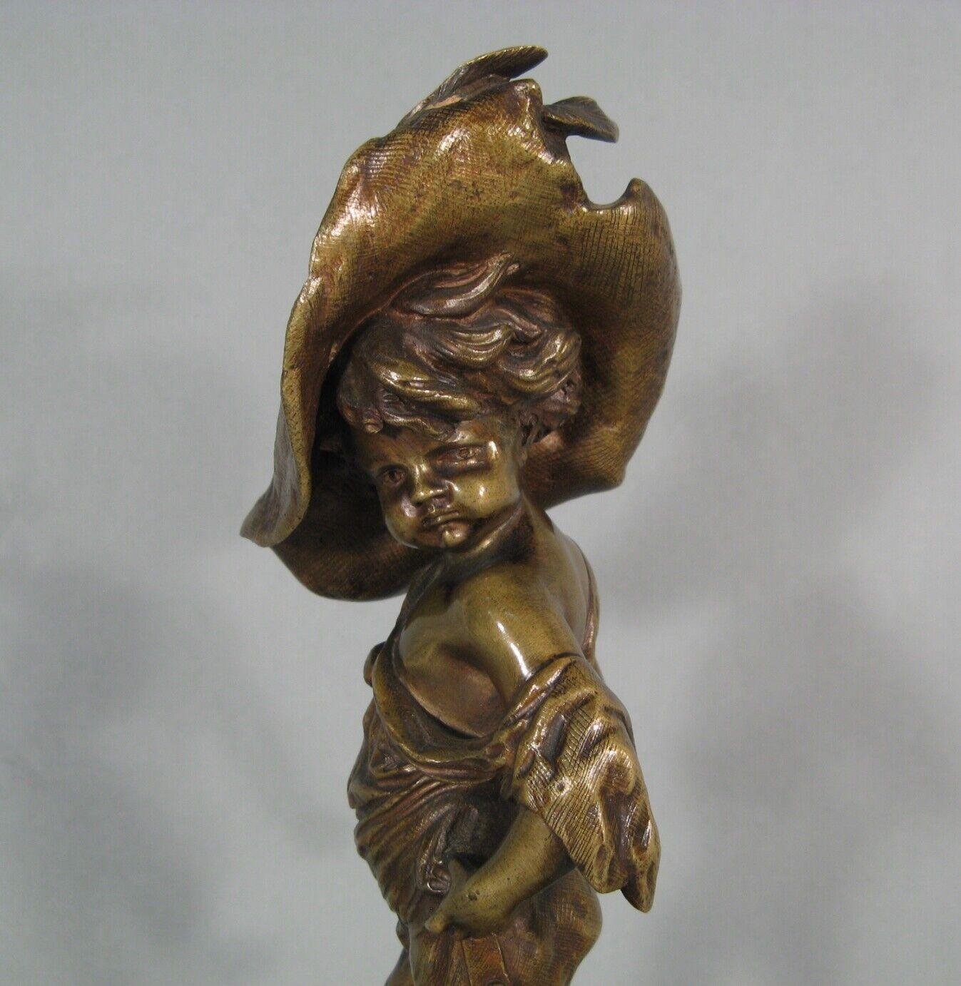 This delightful bronze sculpture depicts a mischievous child wearing a large feathered hat. The piece, which features a patinated finish, is mounted on a red marble base. Although the work is anonymous, it showcases the craftsmanship of the late