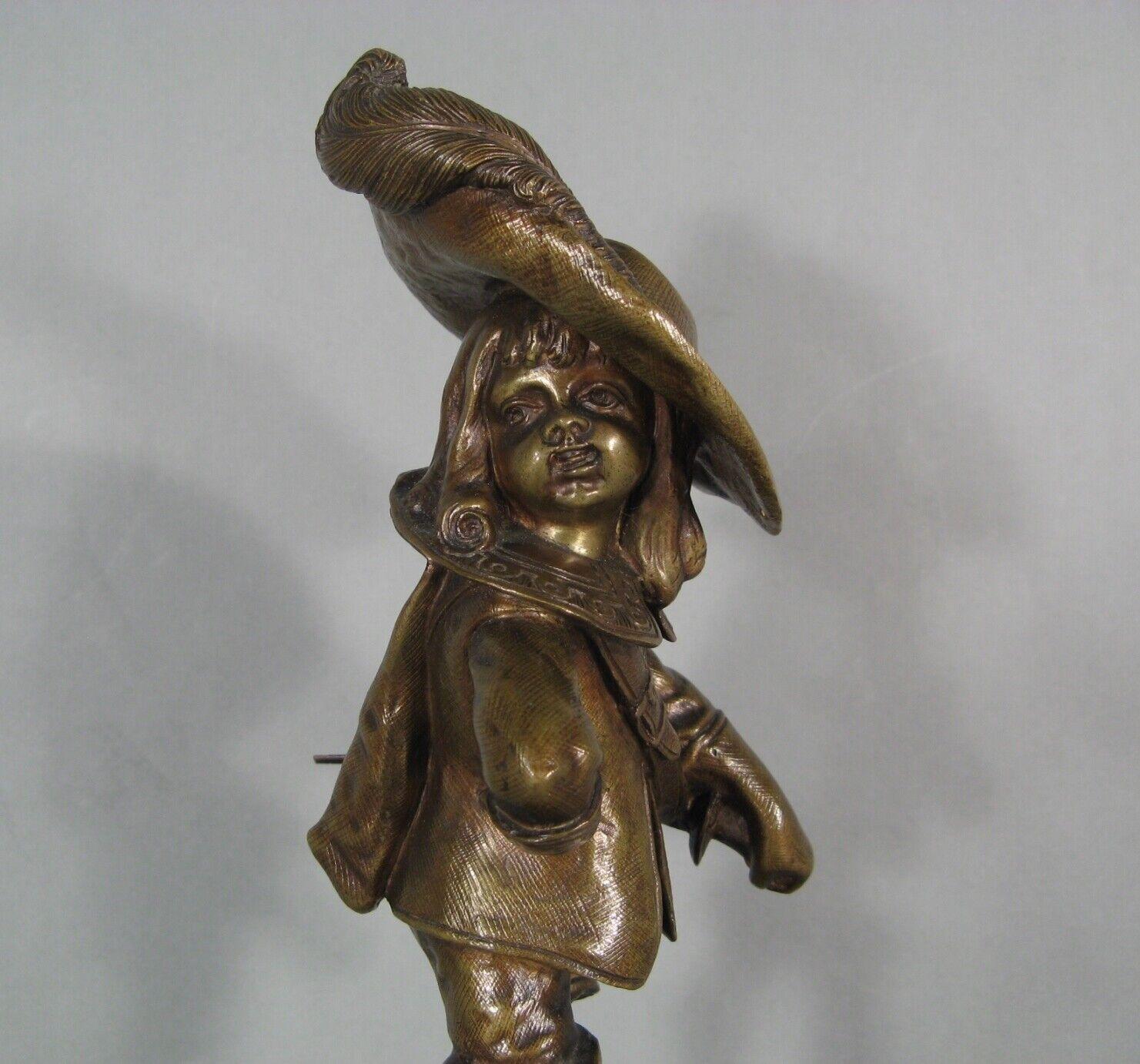 This charming and delightful bronze sculpture depicts a young child dressed as a gentleman, complete with a sword and a musketeer hat. The piece features a patinated finish and is mounted on a red marble base. Although the work is anonymous, it is a
