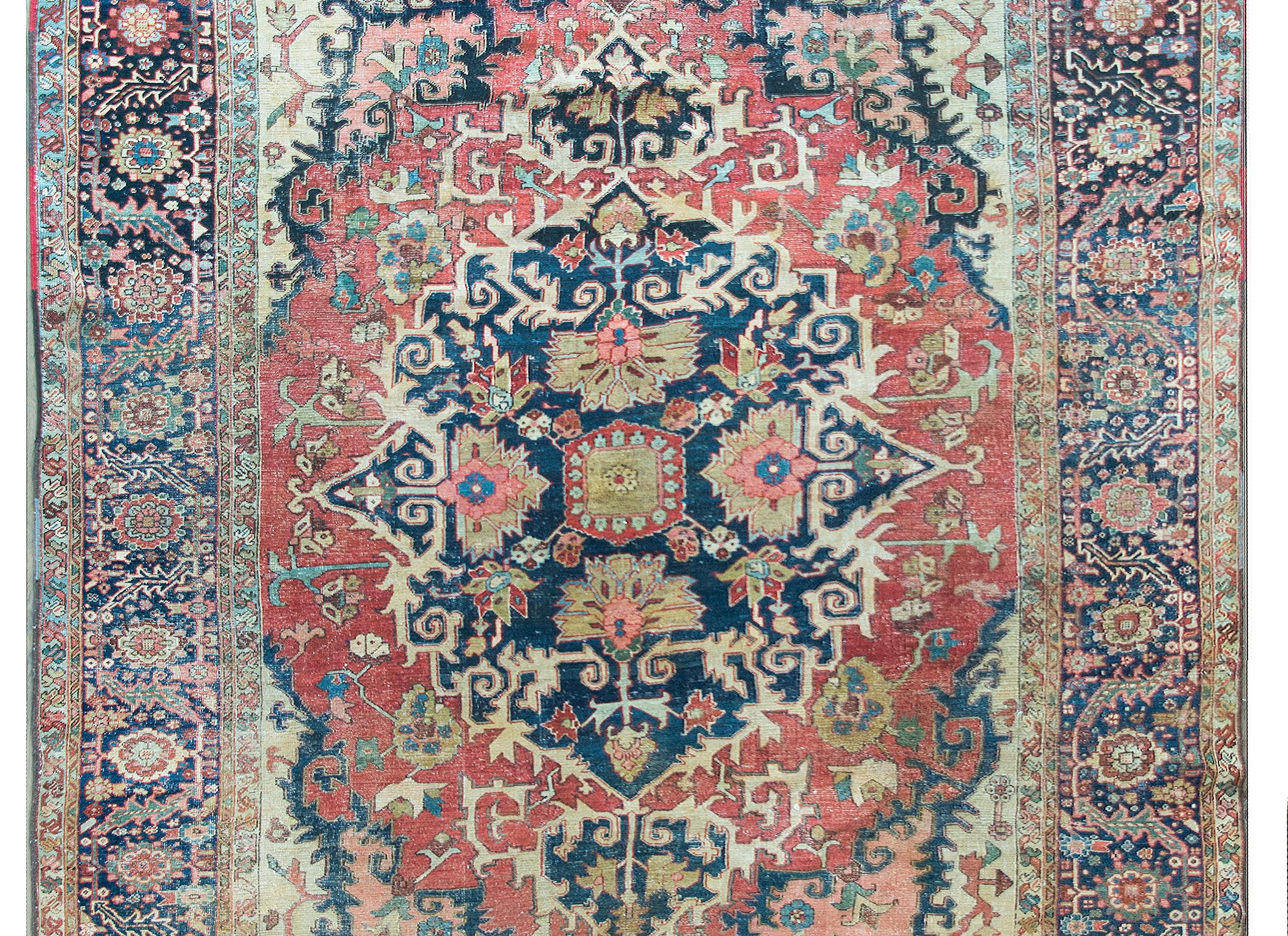 A remarkable and rare late 19th century Persian Heriz Serapi rug with the most wonderful pattern containing a large central medallion with stylized flowers and scrolling vines, woven in crimson, ochre, pink, light indigo, and set against a dark