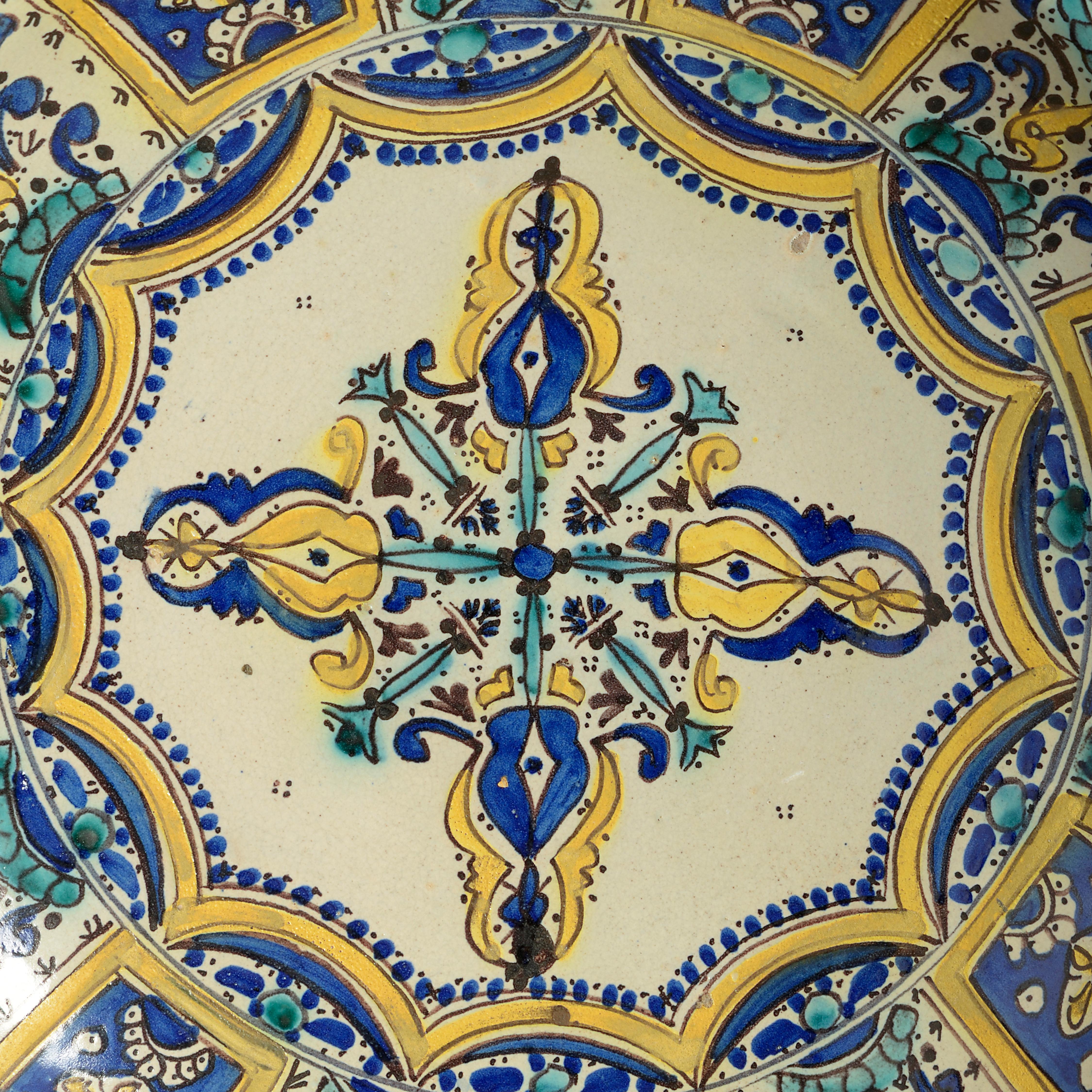 Chargeur en poterie de la fin du XIXe siècle, avec des motifs géométriques en glaçure verte, bleue et jaune sur un fond crème.