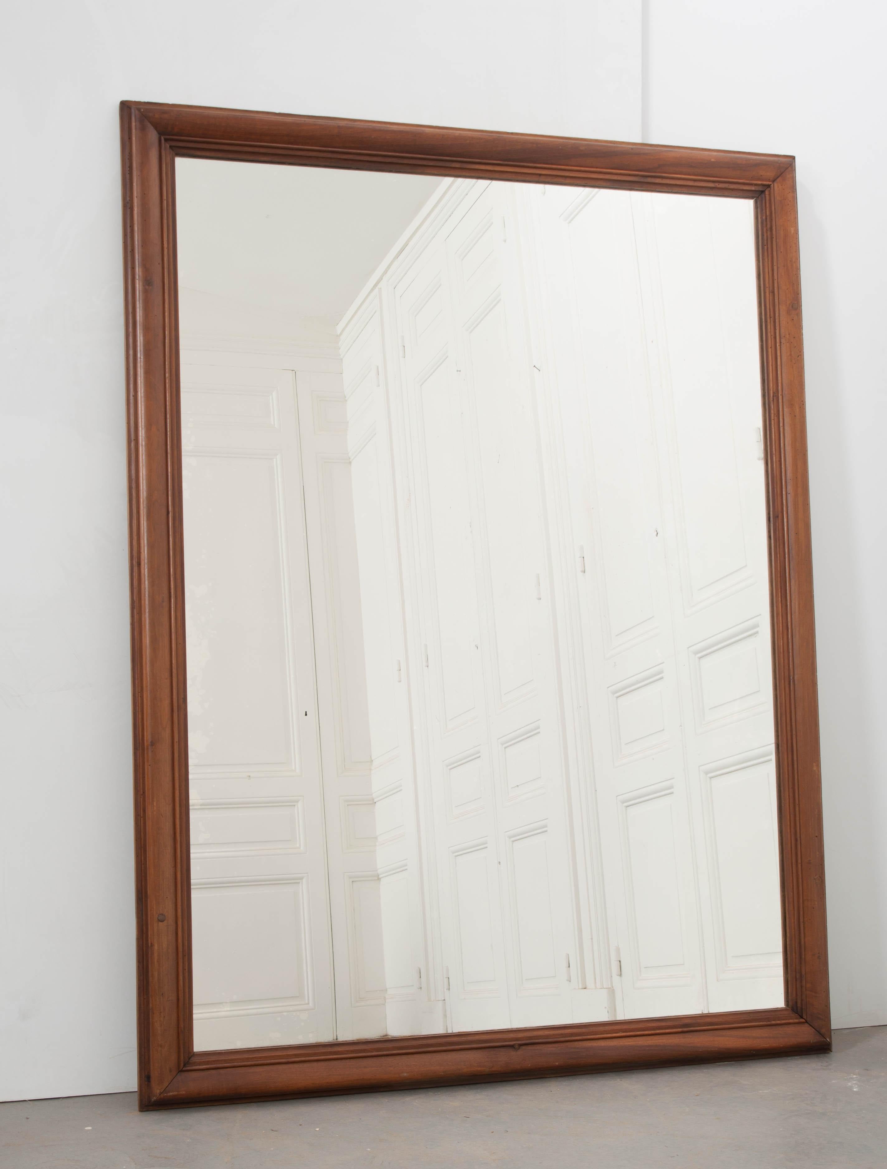 A large carved walnut mirror from France, circa 1890-1900. Uncomplicated yet substantial and attractive, this mirror retains its original glass and is sure to add provincial charm to any room you choose to place it.