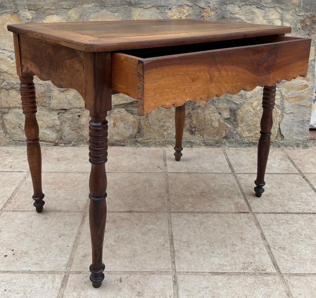 Magnifique table de ferme provinciale de la fin du 19e au début du 20e siècle, fabriquée en noyer massif avec une patine chaude et naturellement vieillie. La pièce présente un charmant tablier festonné et quatre pieds tournés, typiques de