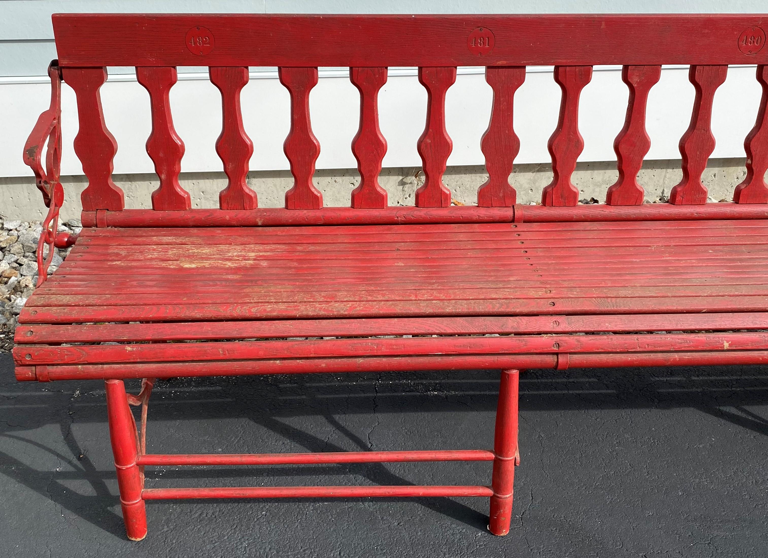 A nice oak folding gymnasium or station bench in red with cast iron hardware that allows the bench to be completely folded and stored when not in use. The back of each seat is numbered, so this was probably used in a gymnasium, auditorium, theater,