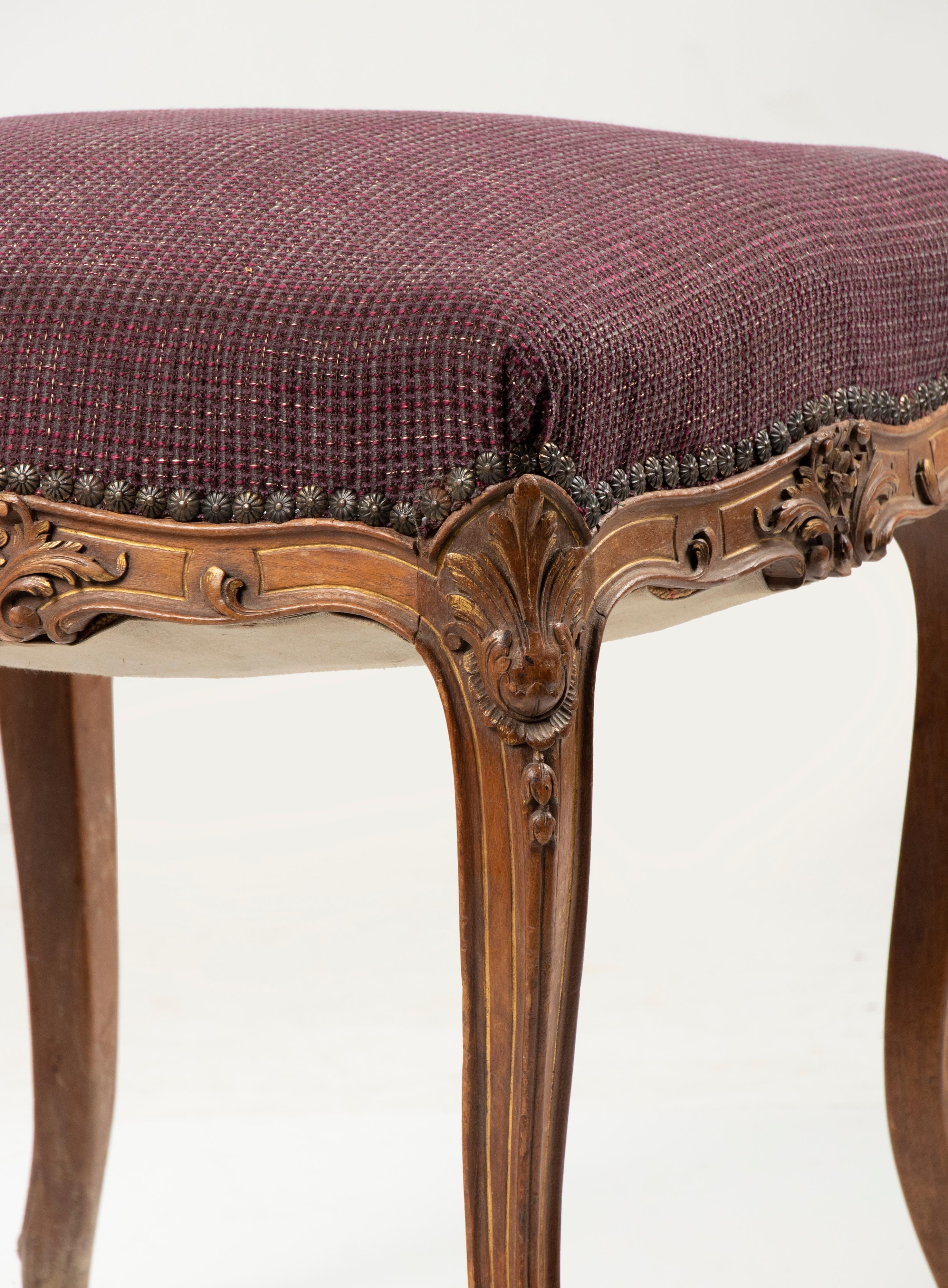 An antique hand carved footstool, made of solid walnut, in the French Régence style. Little gold-colored accents on the carving. The stool has been reupholstered with a deep red fabric. The seat has the original springs. Made in France, circa