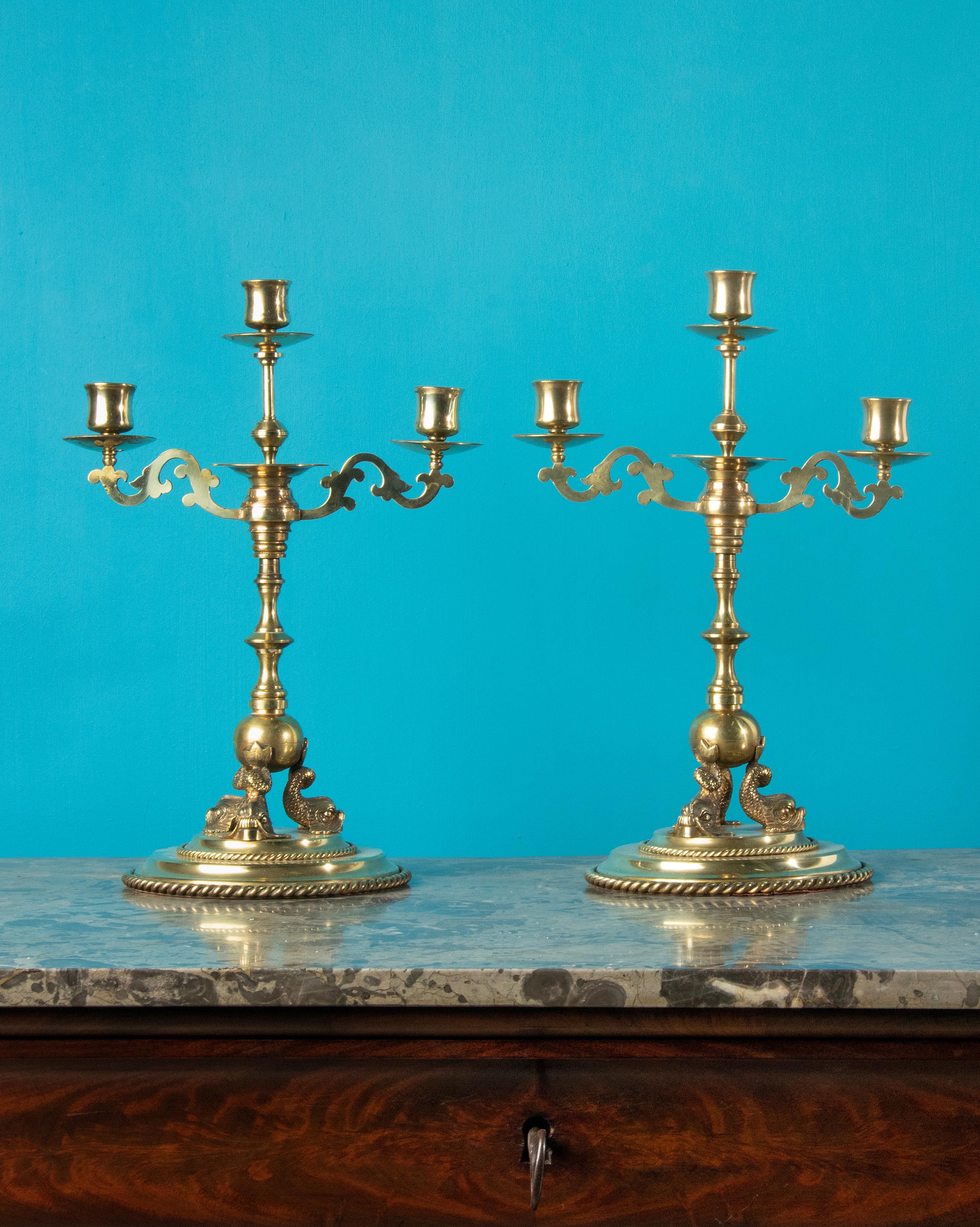 A nice pair of antique candelabras, made of brass. The candelabras have ornate ornaments and dolphins at the base. They date from about 1890. The bottom is covered with red felt. Both are in good condition and have a beautiful color/gloss.