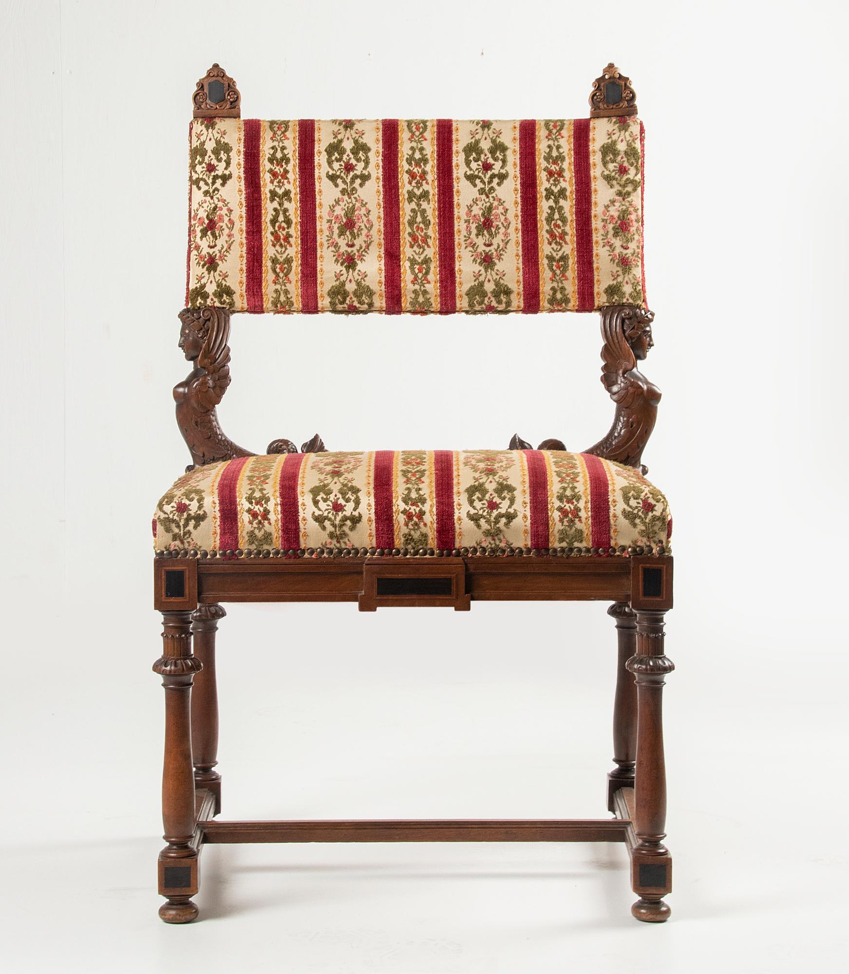 A large antique chair in Renaissance style, also called Henri II style. The chair is made of sculpted walnut wood. Ebonised wood and inlay work on the corners and top ornaments. The back rests on two refined sculpted mermaids. The chair had been