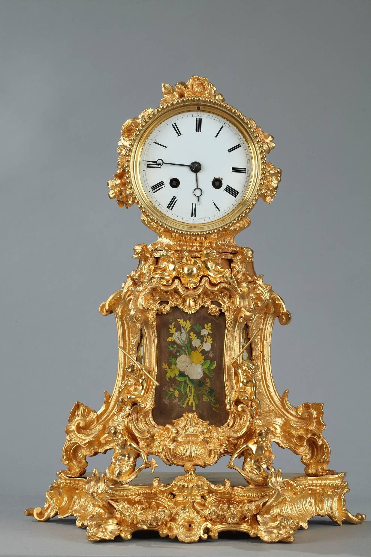 Mantel clock in gilt and sculpted bronze featuring abundant Rocaille motifs such as rinceaux, shells, distressed leaves, and scrollwork. Putti engaged in activities such as reading, fishing, or playing music complete the decor that is characteristic