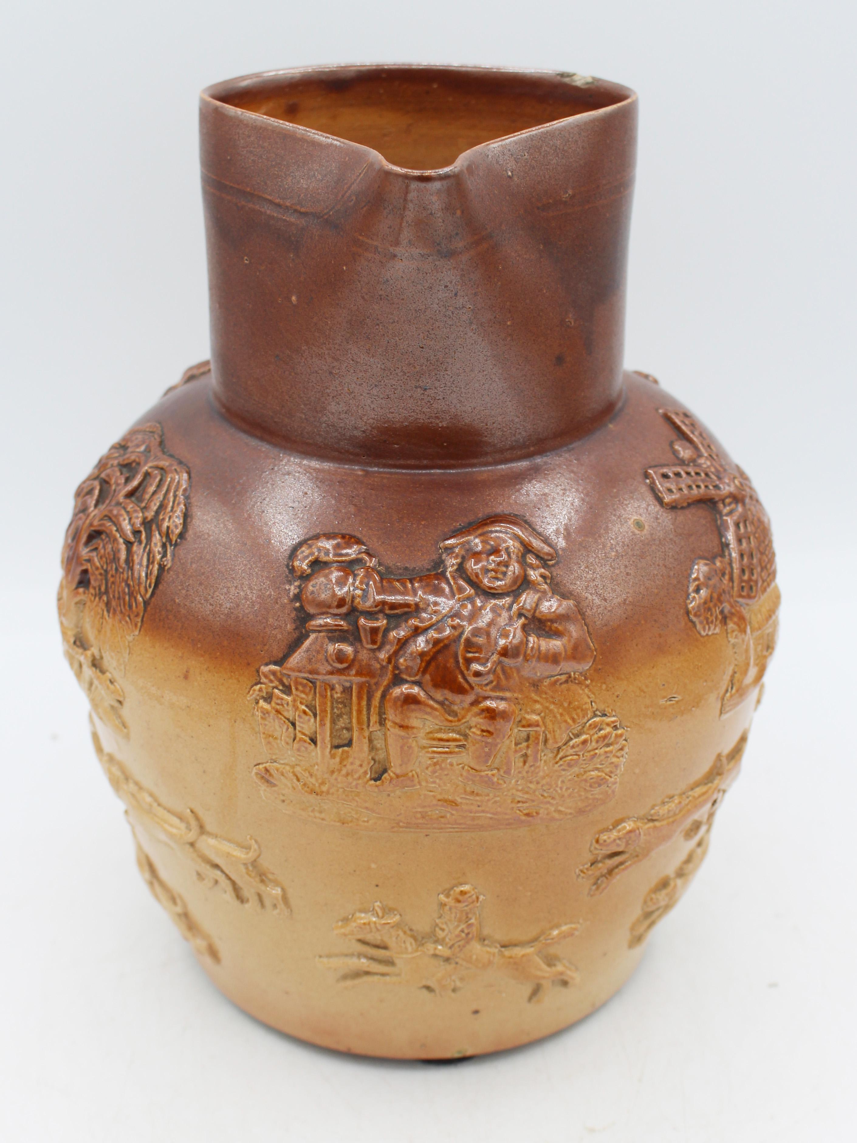 Late 19th century Royal Doulton, Lambeth, London stoneware jug. Molded, applied handle smartly decorated with faux screws & acanthus leaves. Around the body hounds give chase to a stag with hunter on horseback follwing beneath charming vignettes -