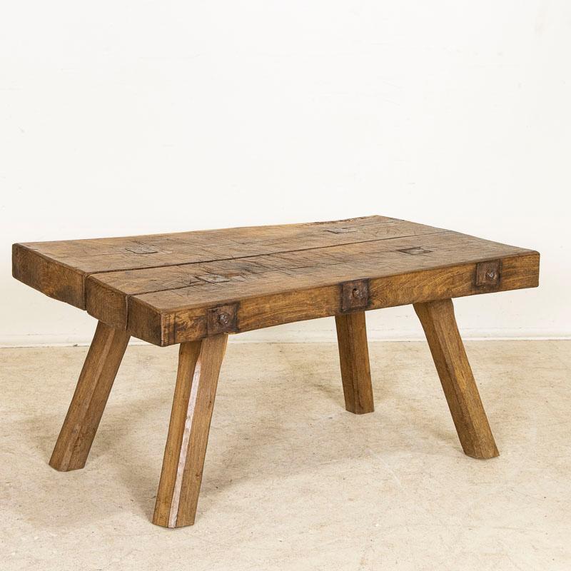 There is something organic and inviting in the thick wood top of this rustic peg leg coffee table. Small but substancial, it is the years of use that have deepened its character with a wonderful worn patina grown richer over time.The heavy gouges,