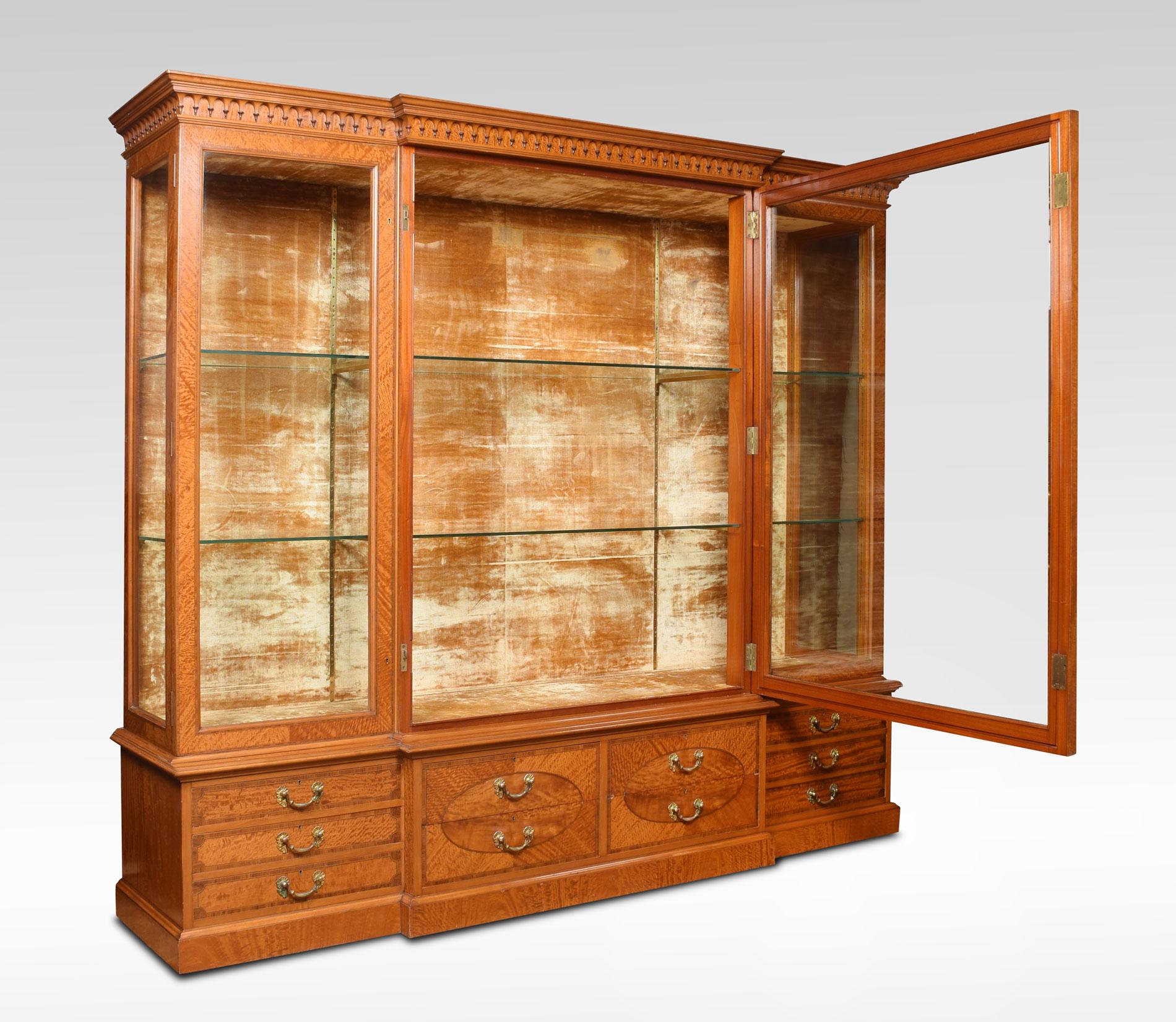 Very large satinwood display cabinet. The moulded cornice with pendant-drop frieze. To the large central glazed door opening to reveal original velvet-lined interior having two adjustable shelves with smaller doors to either end. To the base fitted