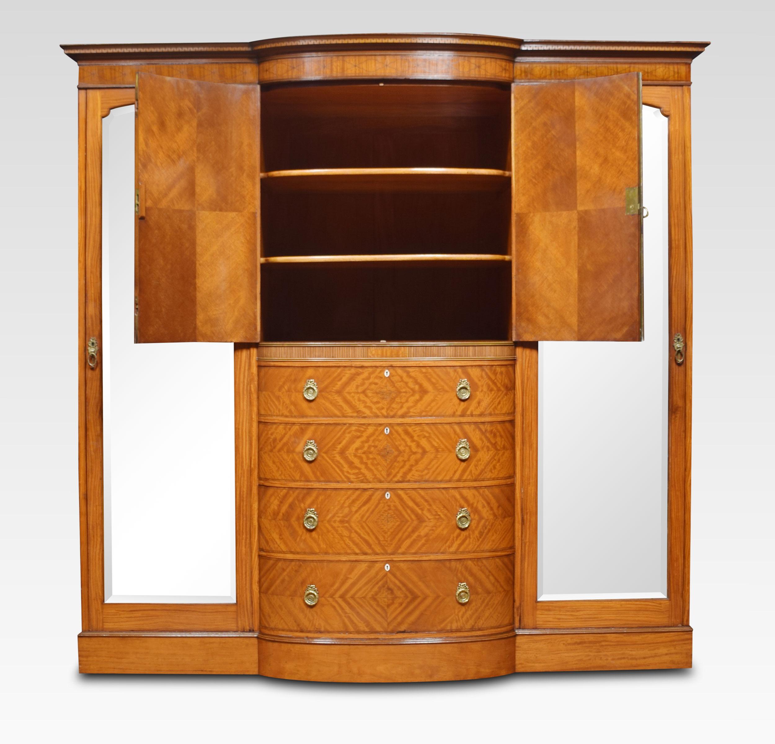 Late 19th century Sheraton Revival bow-fronted compactum wardrobe, the detachable decorated cornice above a central cupboard fitted with bow-fronted shelves enclosed by a pair of floral inlaid panel doors. Above four long graduated drawers. Flanked