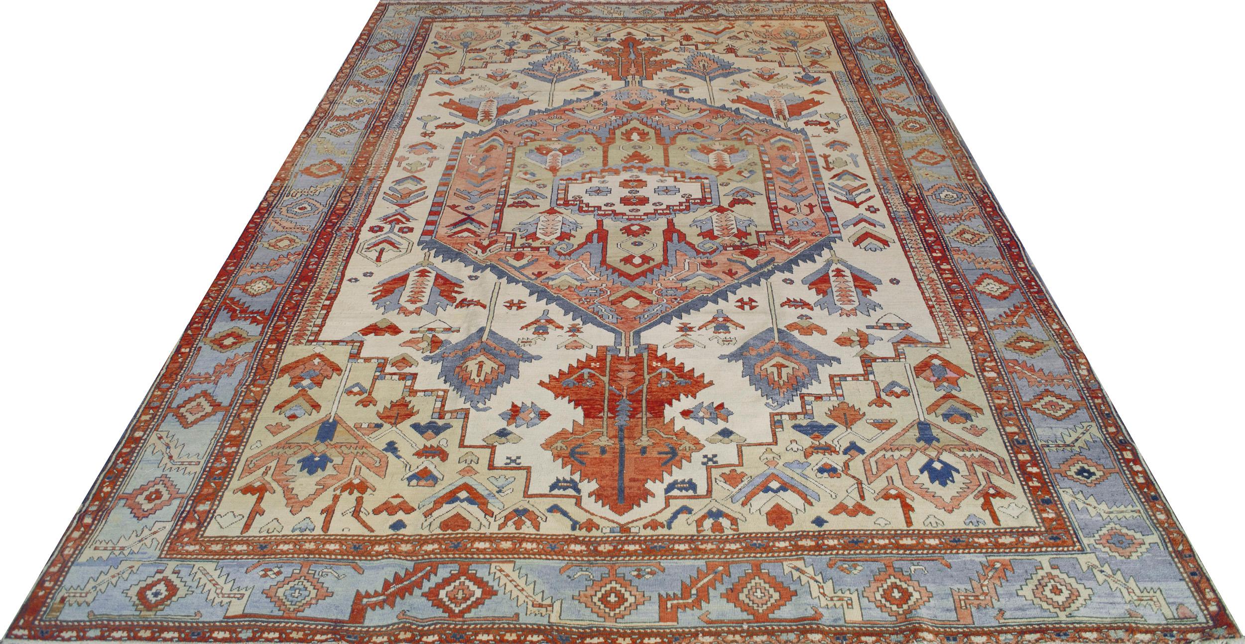 This traditional handwoven Persian Serapi rug has an ivory field with broad serrated floral motif enclosing a grand shaded coral stylized medallion of similar geometry, in broad beige stepped spandrels, and a soft sapphire geometric linked border,