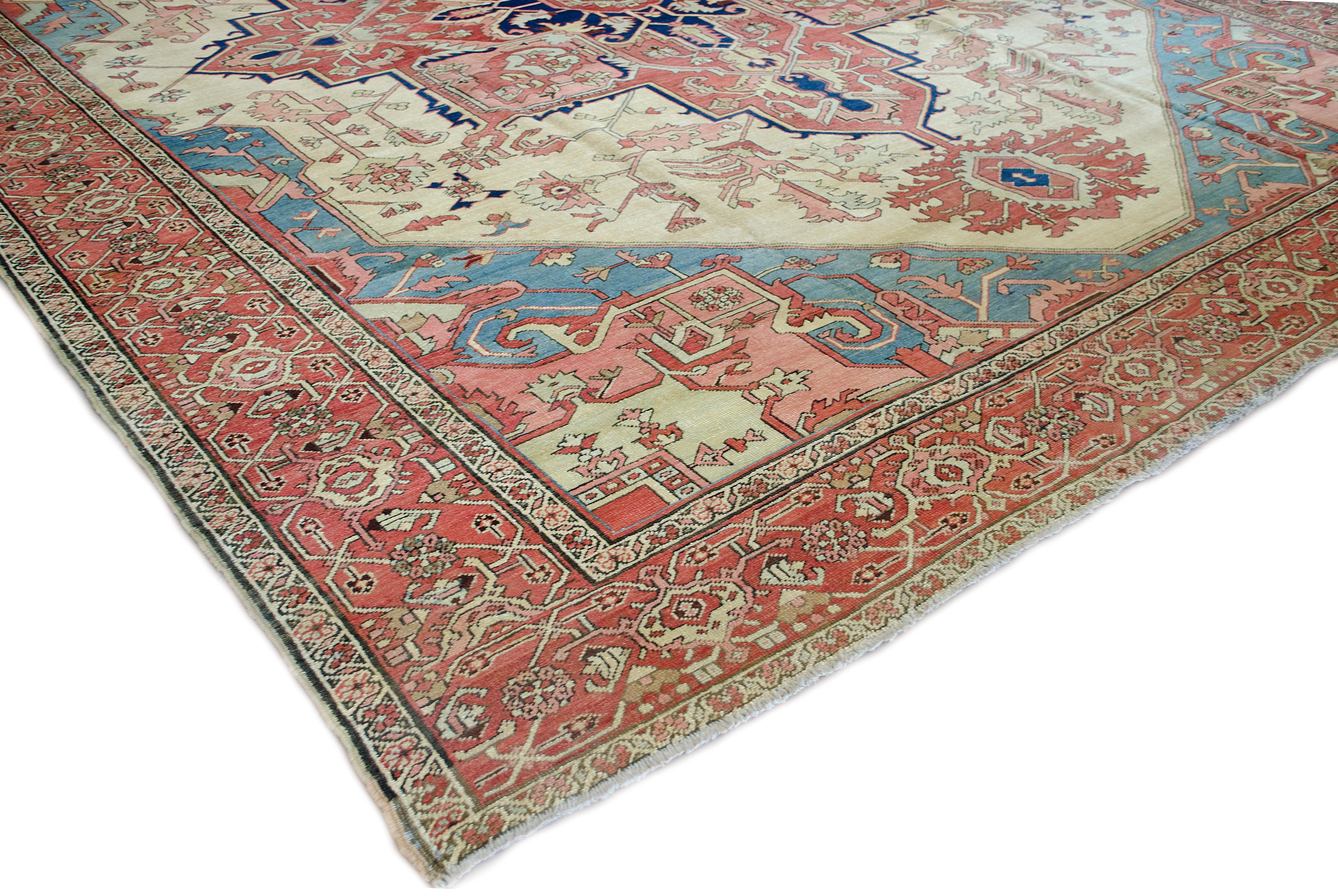 This traditional handwoven Persian Serapi rug has a warm beige field of angled palmette vines and tendrils enclosing a magnificent ruby rust radiating lozenge medallion enclosing similar geometric floral motif and inner indigo arabesque issued by