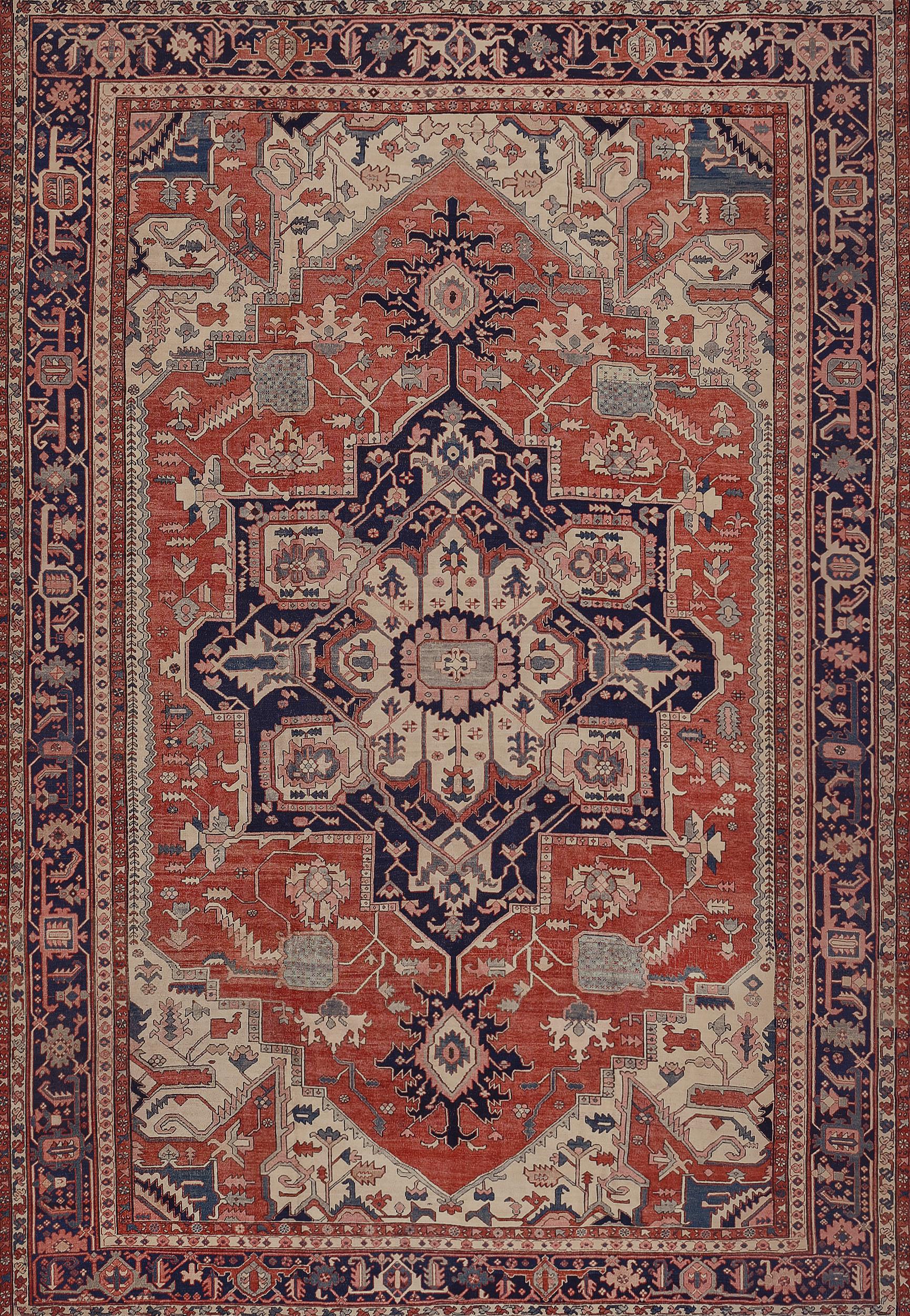 This traditional handwoven Persian Serapi rug has a shaded coral red field of sparse angled geometric palmettes vines, enclosing an imperial indigo lozenge medallion, with reciprocal ivory spandrels, in an indigo geometric turtle palmettes border,