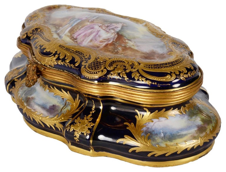A very stylish and decoration late 19th Century French Sevres style porcelain casket. Having a Cobalt Blue ground with wonderful scrolling gilded decoration, inset hand painted panels depicting various rural scenes and one to the lid of lovers