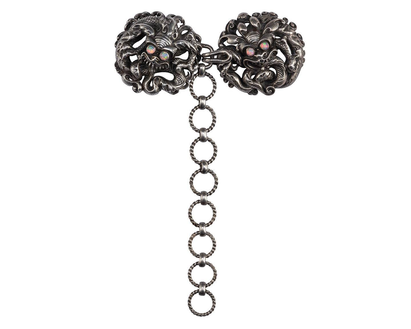 Louis Wièse 
Cape Clasp 
France (Paris), c. 1890
Silver, opals
Weight 102.8 gr.; Length 22.23 cm.; individual clasp diameter(s) c. 44 mm.

Two openwork roundels in relief show a Chinese dragon head in cast and chased silver, entwined by a serpentine