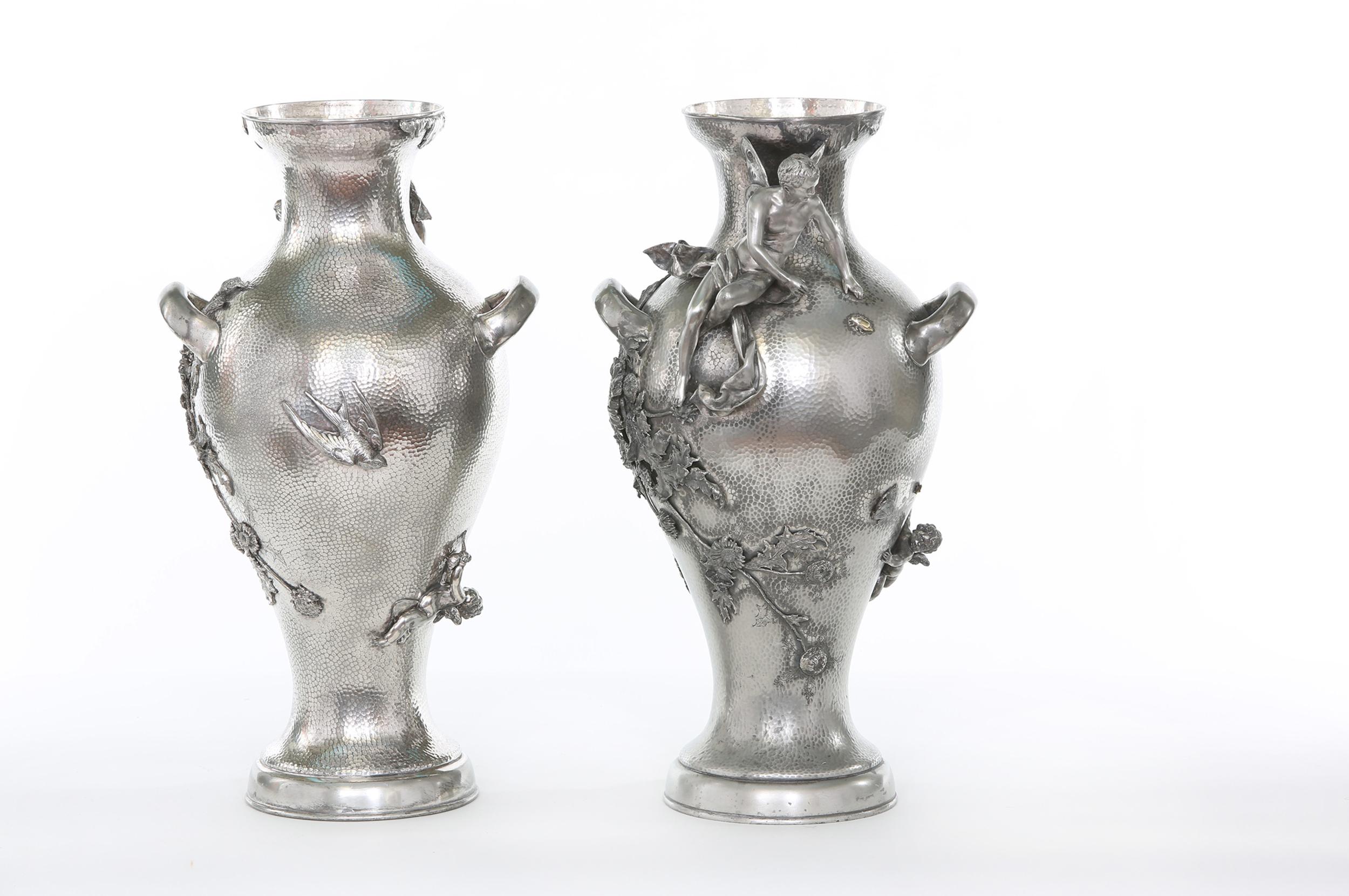 Late 19th century silver plated pair of handcrafted decorative vases / urns with exterior design details and removable water holder receptacle. Each vase / piece is in great condition. Minor wear consistent with age / use. Each vase stands about 20