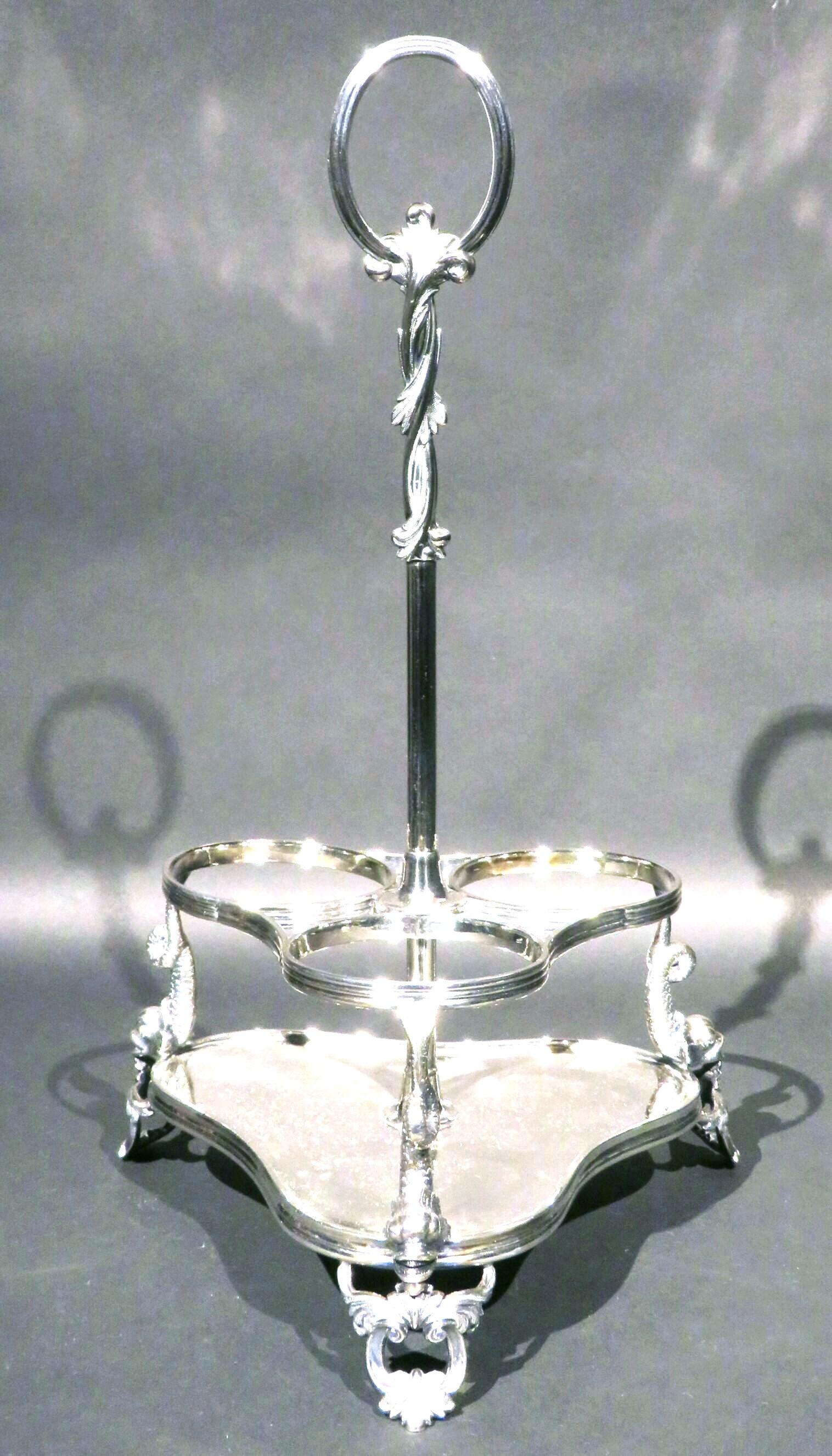 Un bellissimo portabottiglie da vino in argento placcato, con una base a tre angoli con bordatura, dotata di una galleria che accoglie in modo sicuro 3 bottiglie di vino a forma di Bordeaux, sollevata su tre supporti a forma di delfino e dotata di